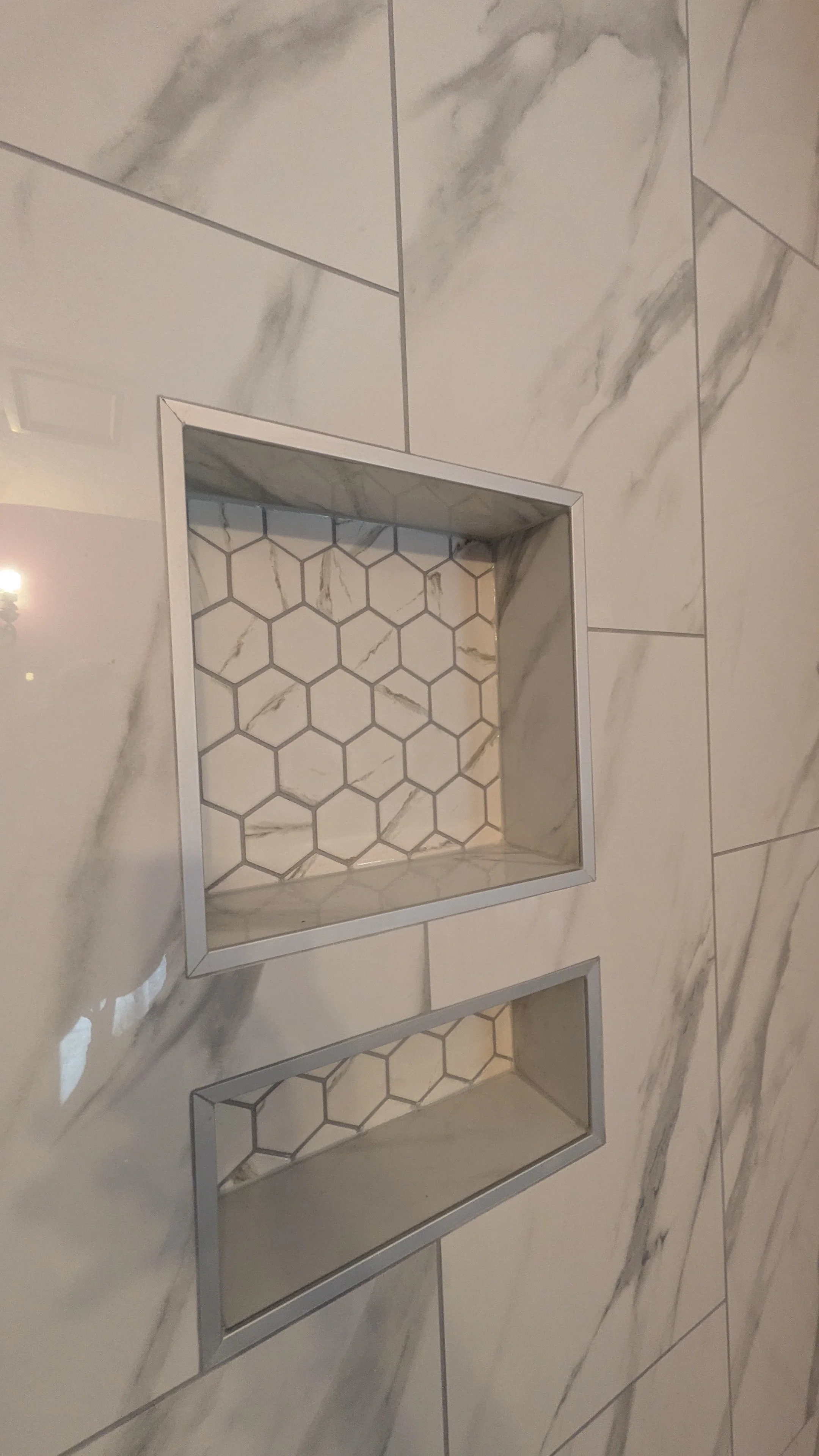 Two rectangular, niche-style shelves with hexagon tile backgrounds, set into a marble tile wall.