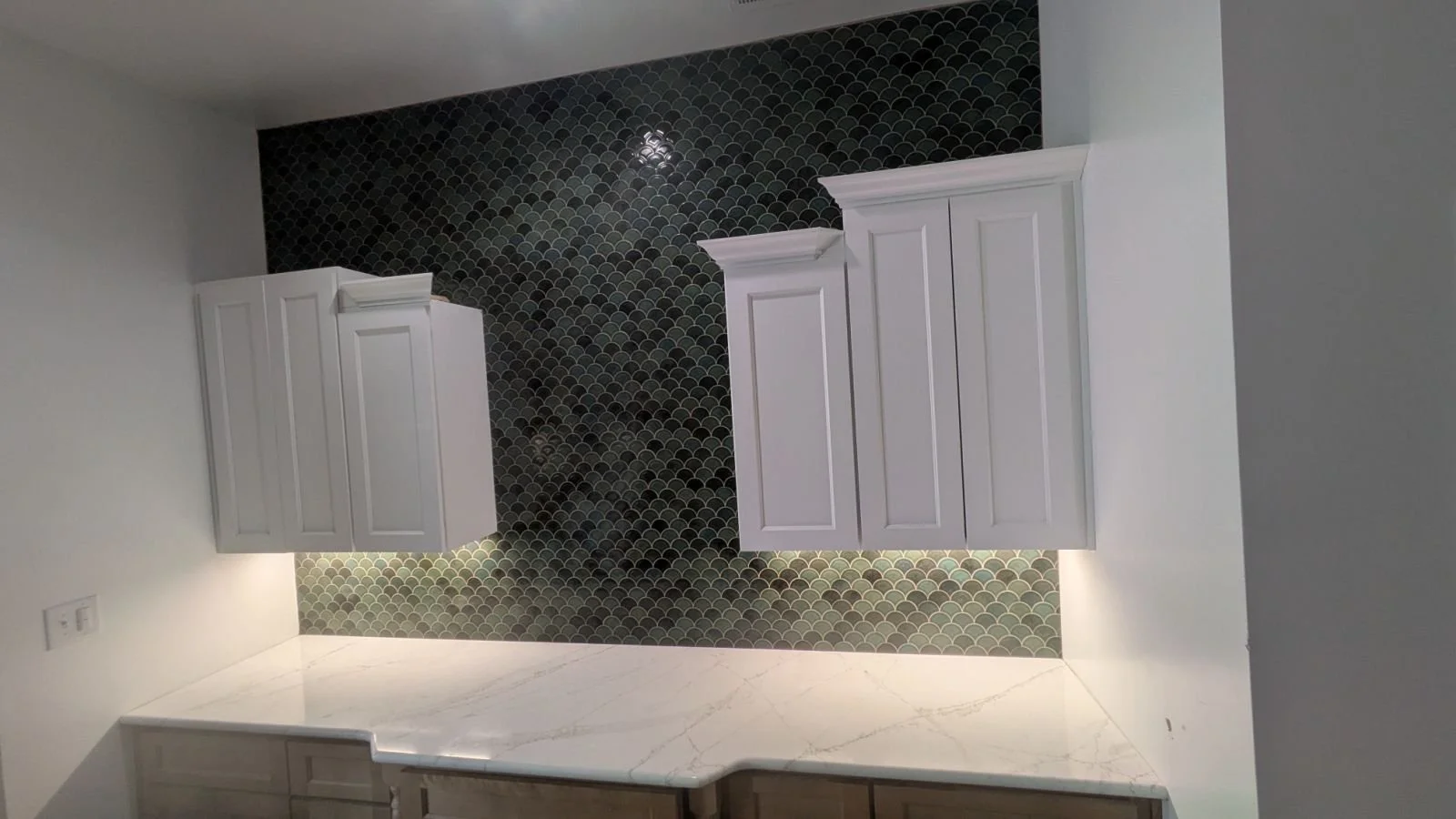 Kitchen with white cabinets, a white marble countertop, and dark patterned tile backsplash.