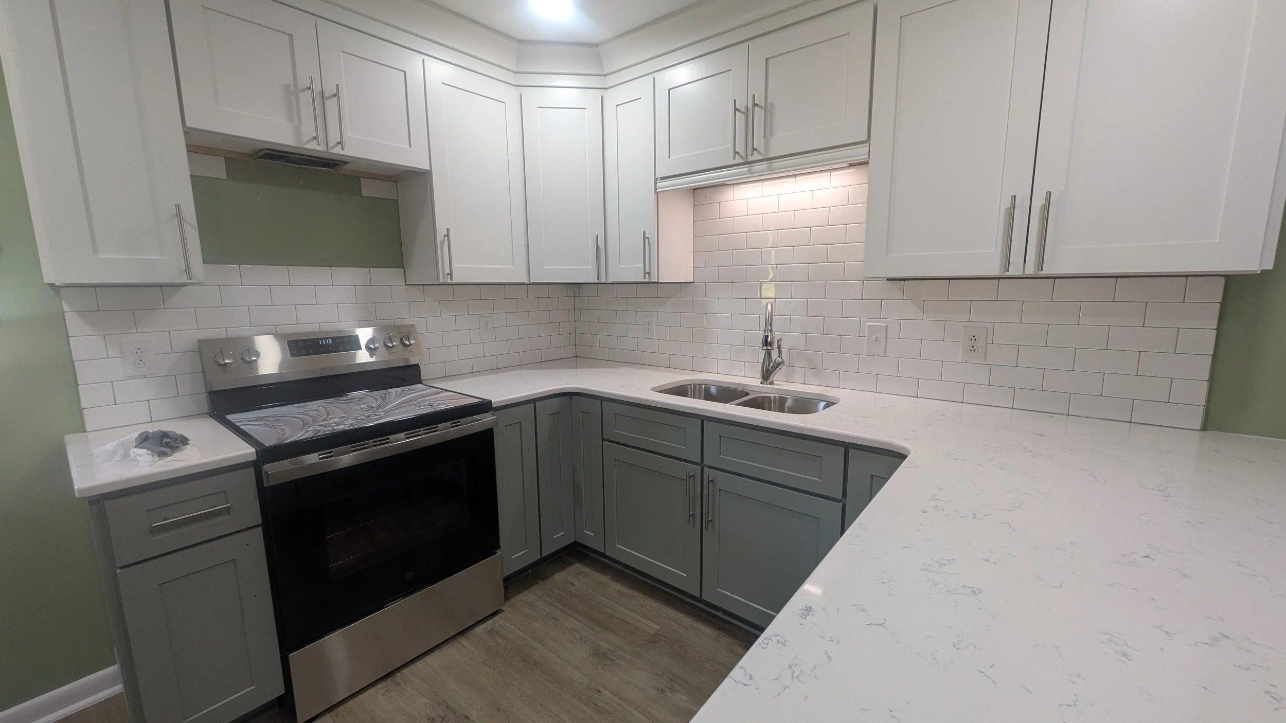 Modern kitchen with white upper cabinets and gray lower cabinets, white marble countertop, stainless steel stove, white subway tile backsplash, and a double sink.