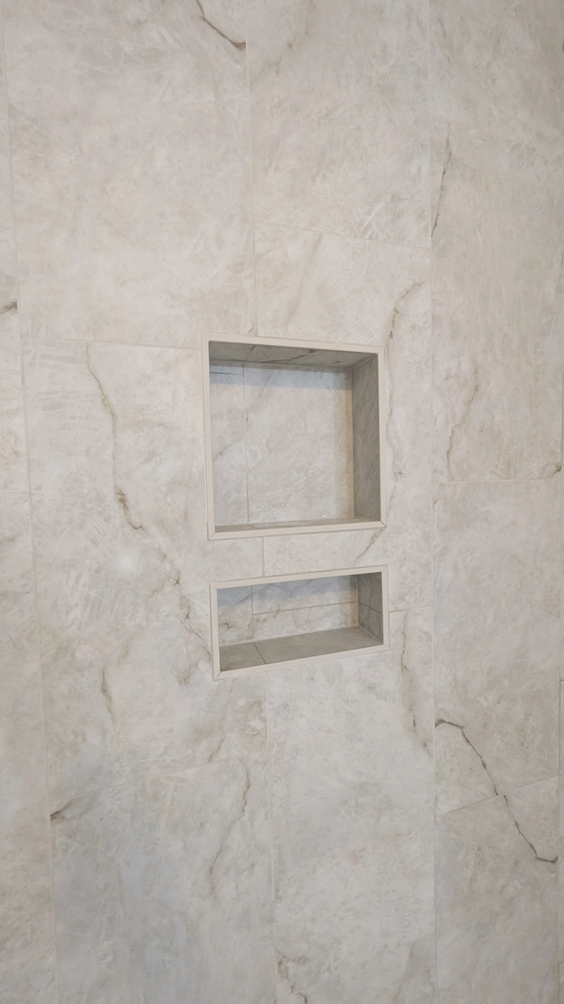 Close-up of tiled wall with two recessed shelves in a bathroom or shower area.