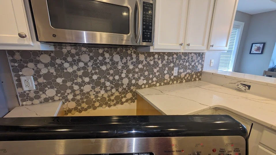 Kitchen countertop with a microwave overhead, a mosaic tile backsplash, and a stove in the foreground.