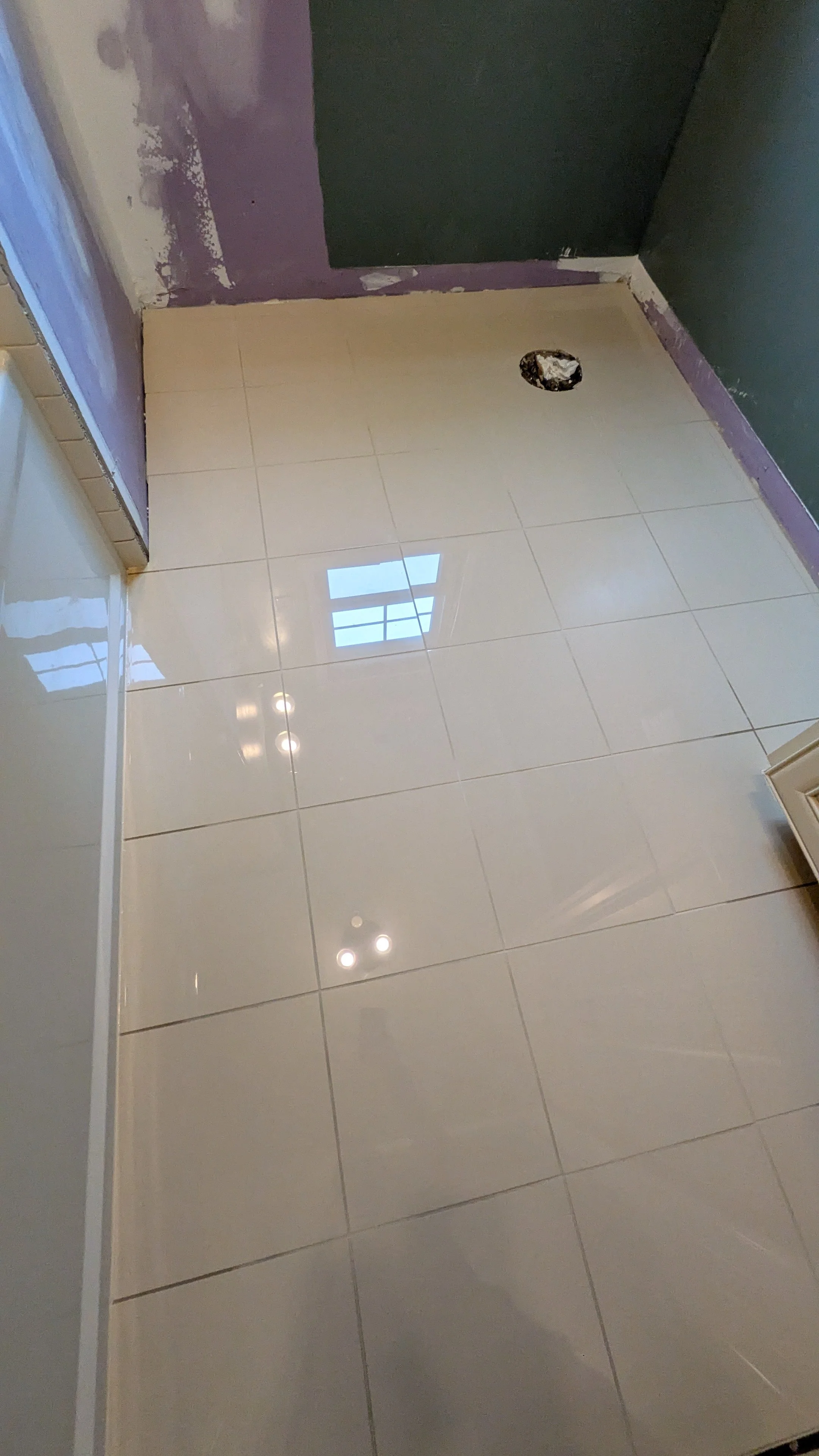 Clean tiled floor in a room under renovation with visible wall repairs and a floor drain hole.