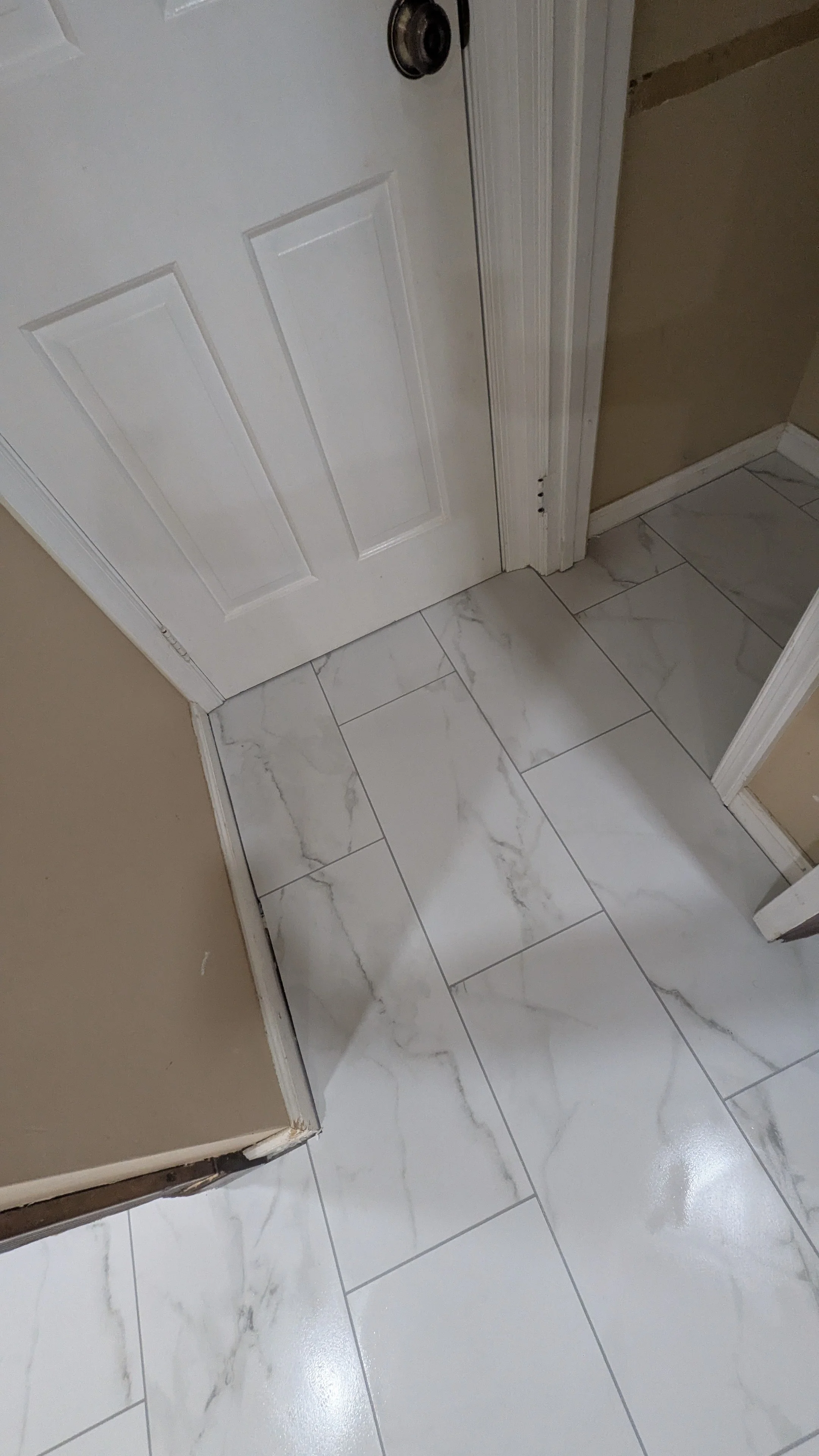 View of a white door, beige walls, and a floor with large white marble-patterned tiles.