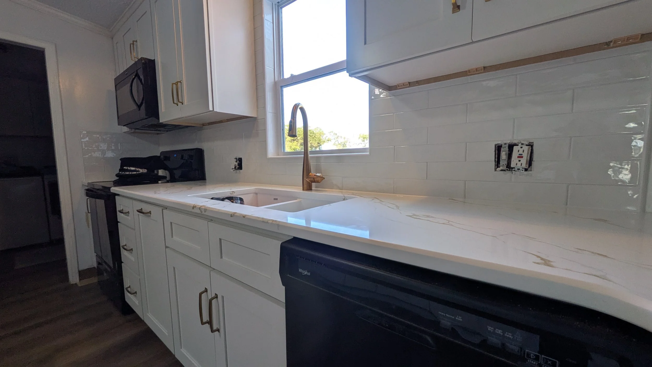 Kitchen with white cabinets, a window above the sink, a black microwave, a black stove, and a black dishwasher, with a marble countertop and a tiled backsplash.