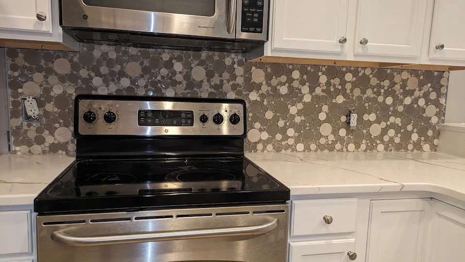 Kitchen with a black and stainless steel electric stove and oven, white cabinets, a microwave above, and a patterned tile backsplash with circles in grey and white.