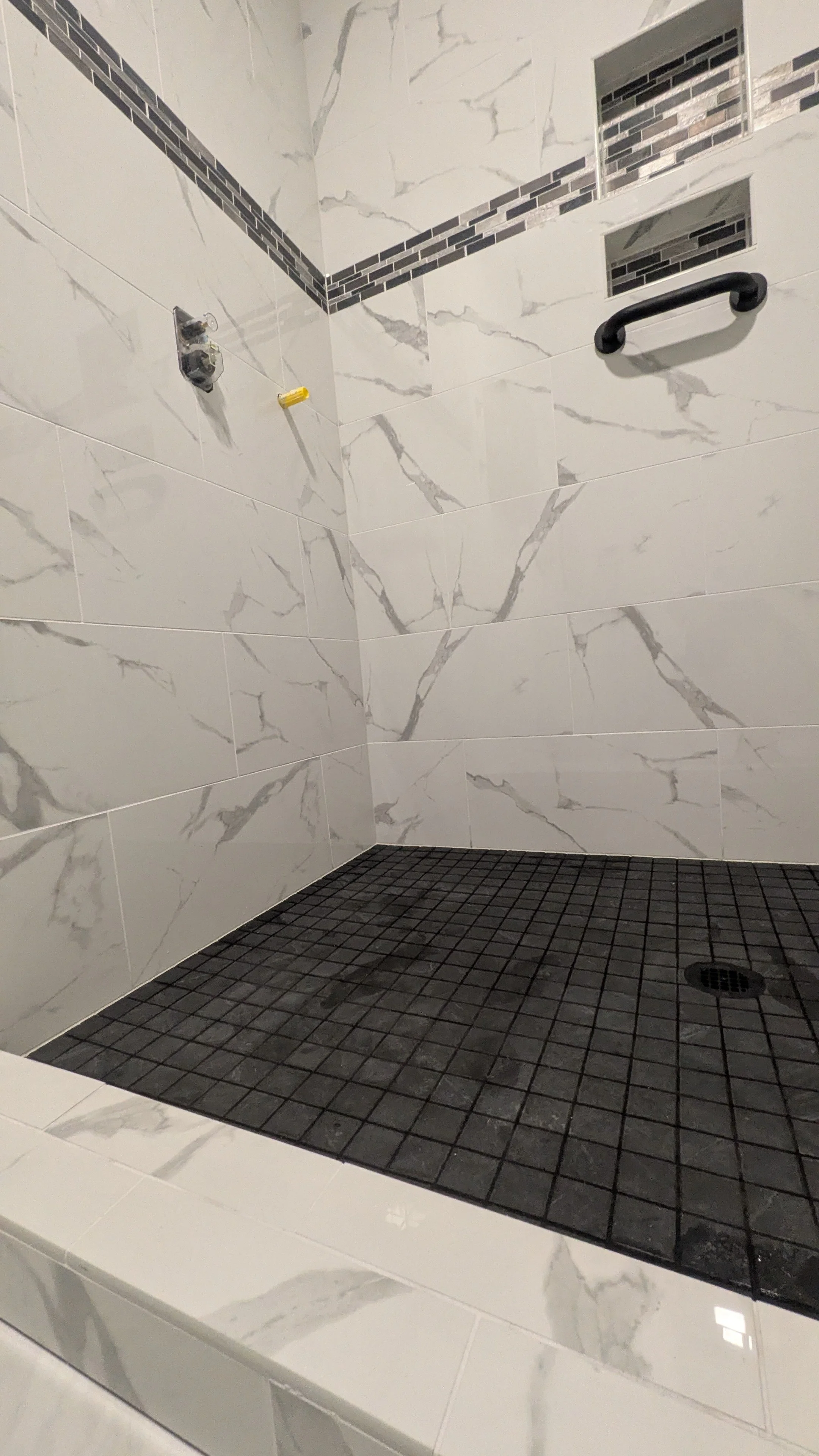 Empty walk-in shower with marble walls, black tile floor, and built-in shelves.