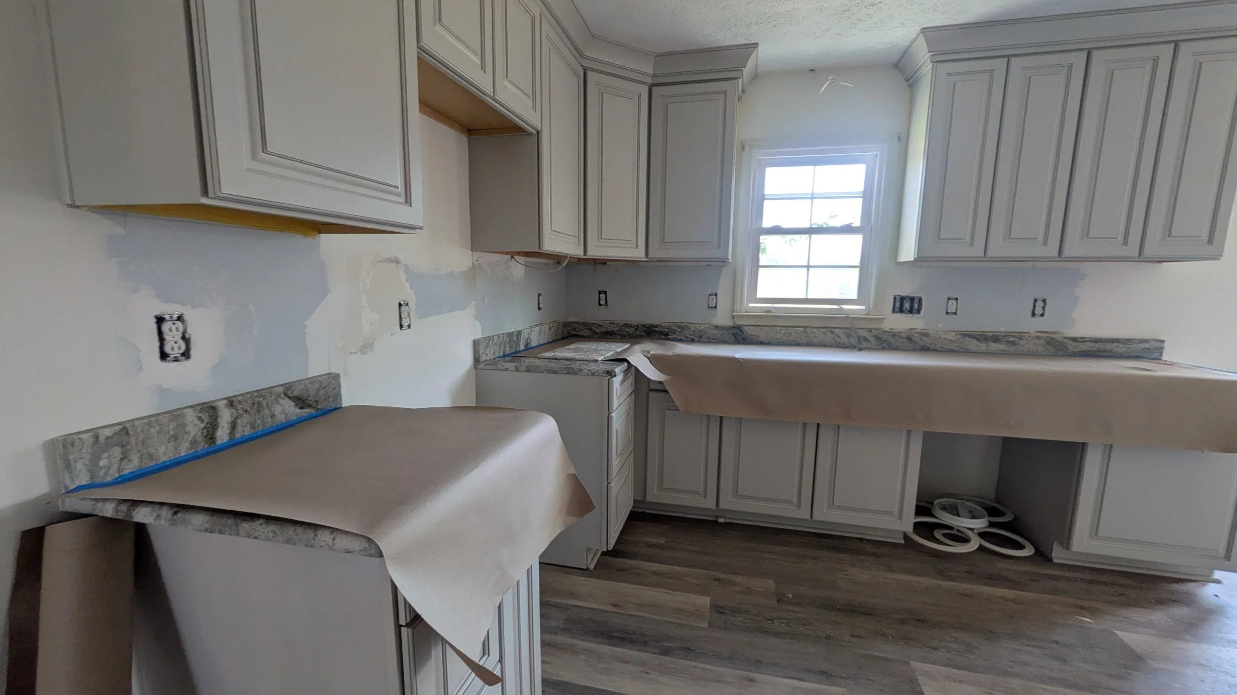 Kitchen under renovation with unfinished cabinets, exposed outlets, and protective paper on the countertops.