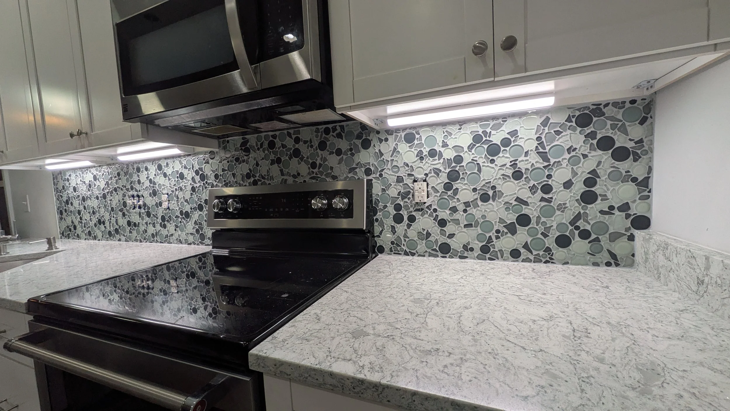 Kitchen with gray cabinets, granite countertop, mosaic tile backsplash, microwave oven, and electric stove.