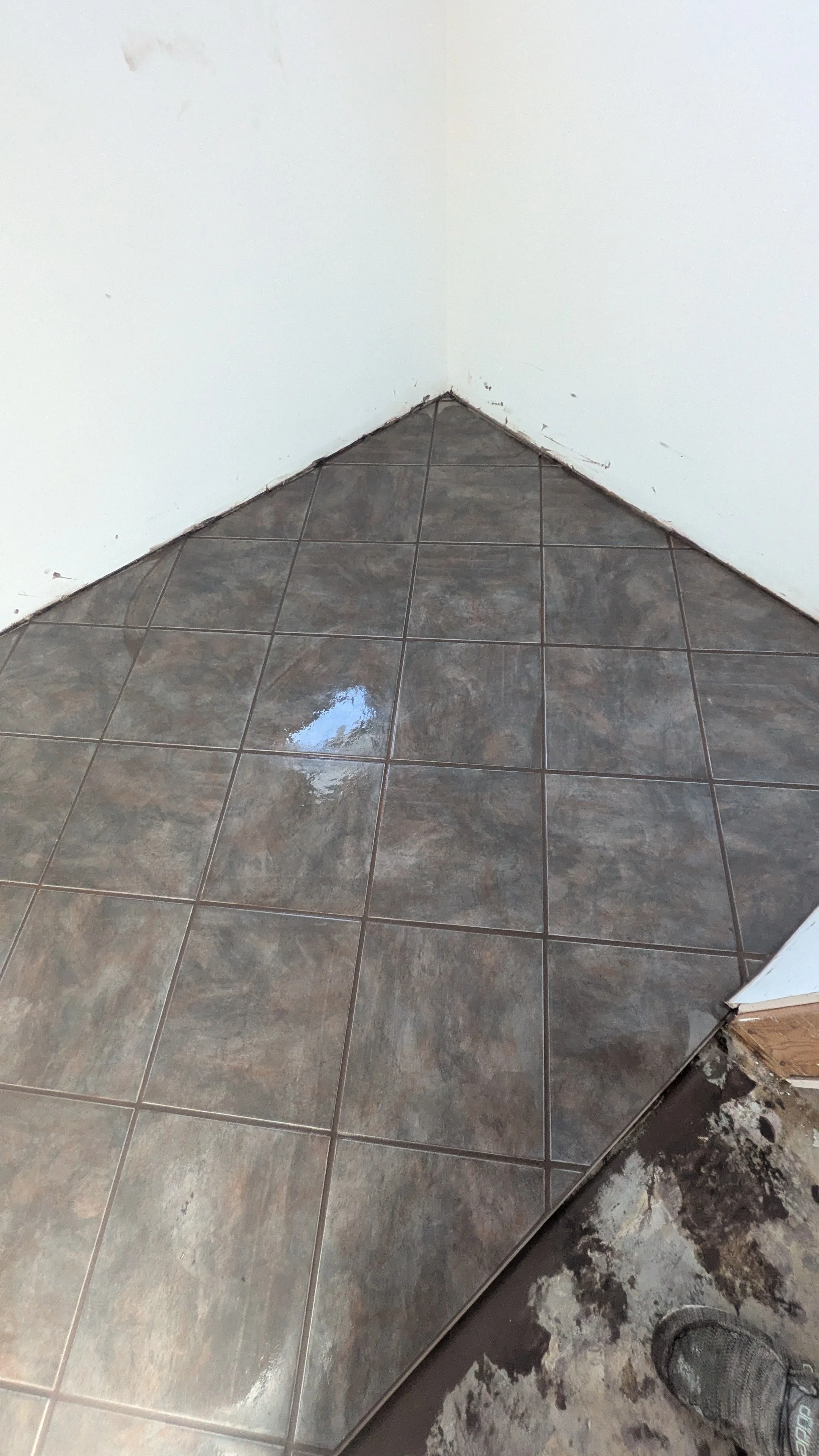 Corner of a room with tiled floor and white walls, some dirt and damage visible on the walls and floor.