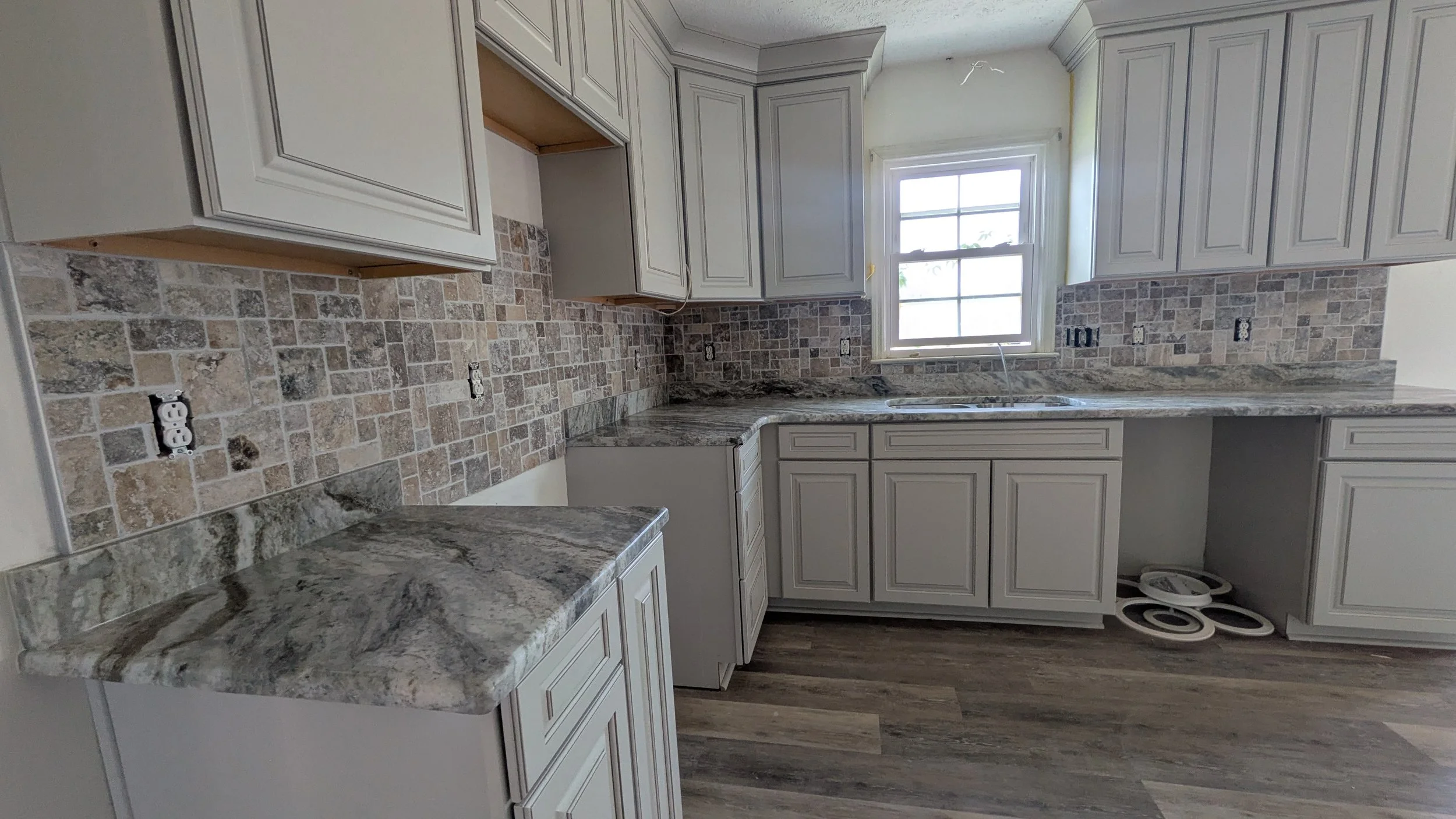 Kitchen with white cabinets, marble countertops, and a stone tile backsplash under a window.