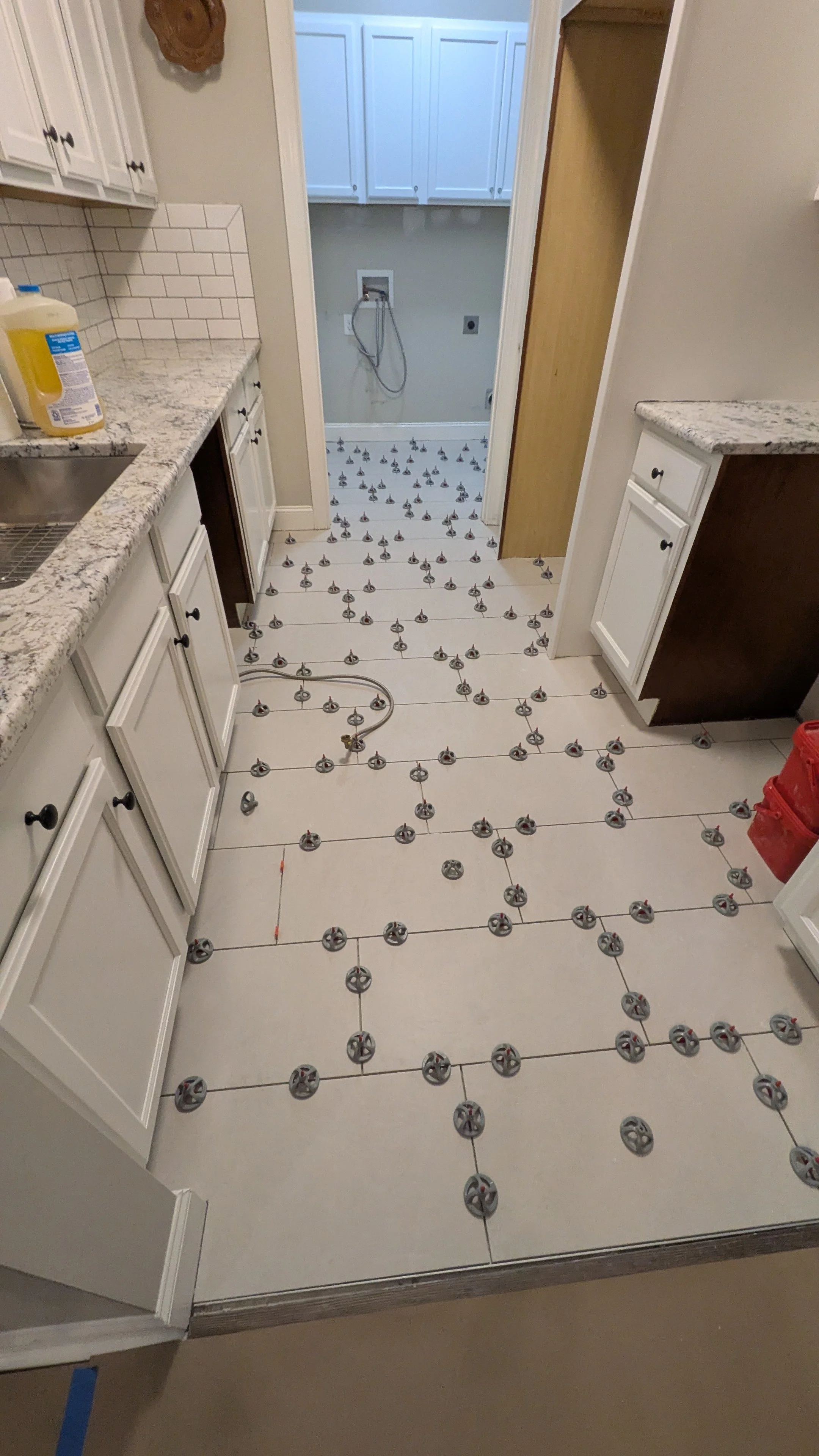 Kitchen floor with underlayment and tiles being installed, with tiles arranged and spacers in place.