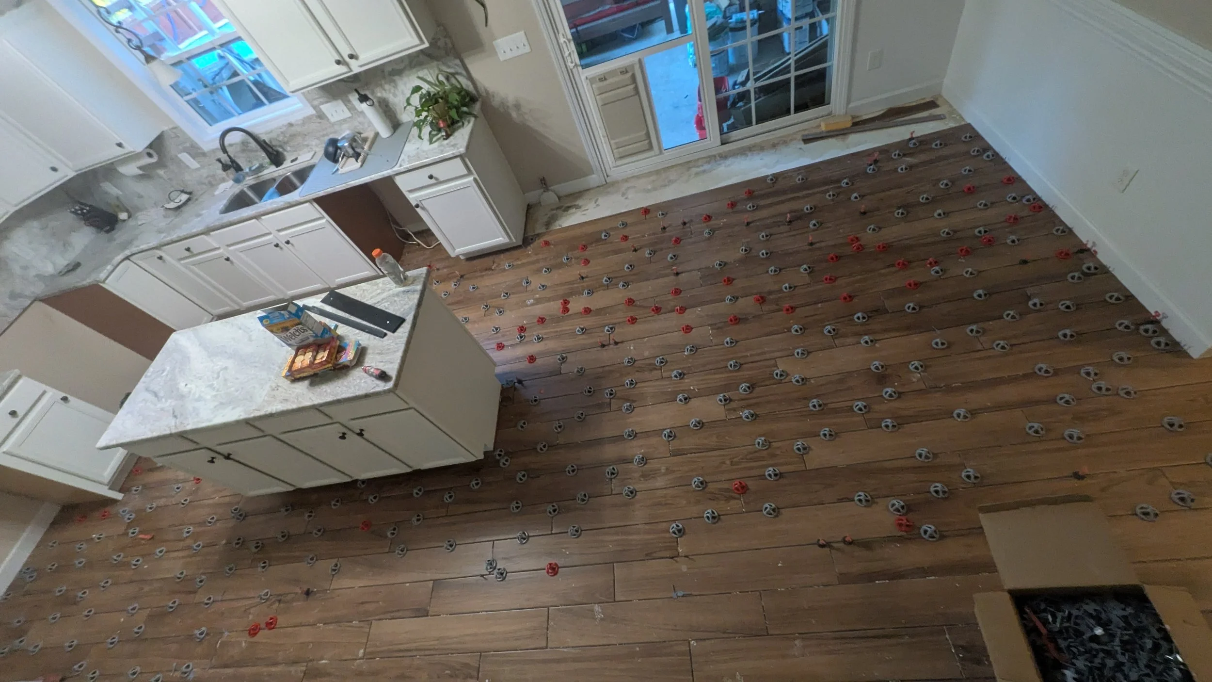 Kitchen under renovation with hardwood floor and underfloor heating system installation in progress, showing numerous heating cable clips on the floor.