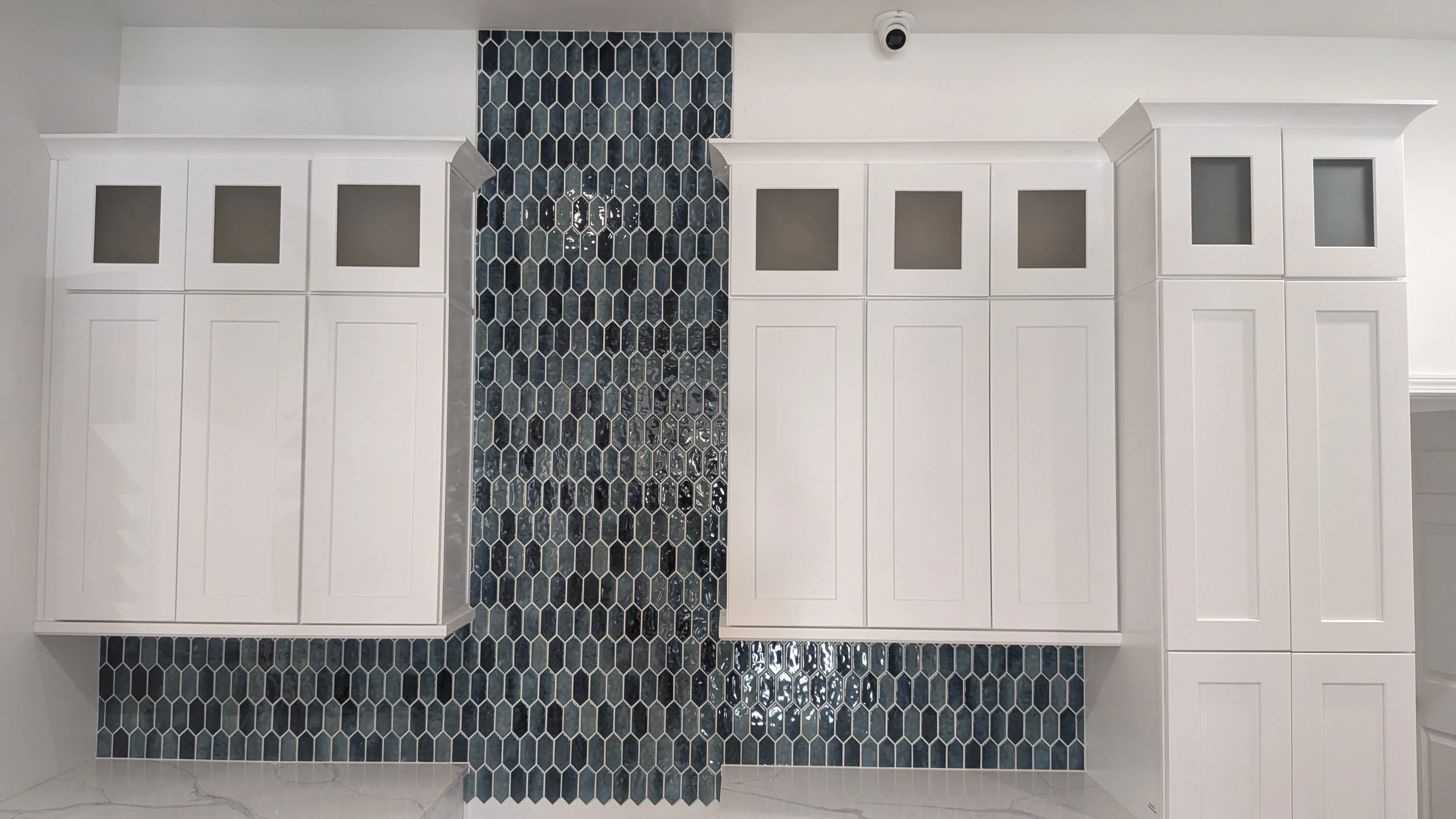 White kitchen cabinets with frosted glass panels and a blue hexagon tile backsplash.