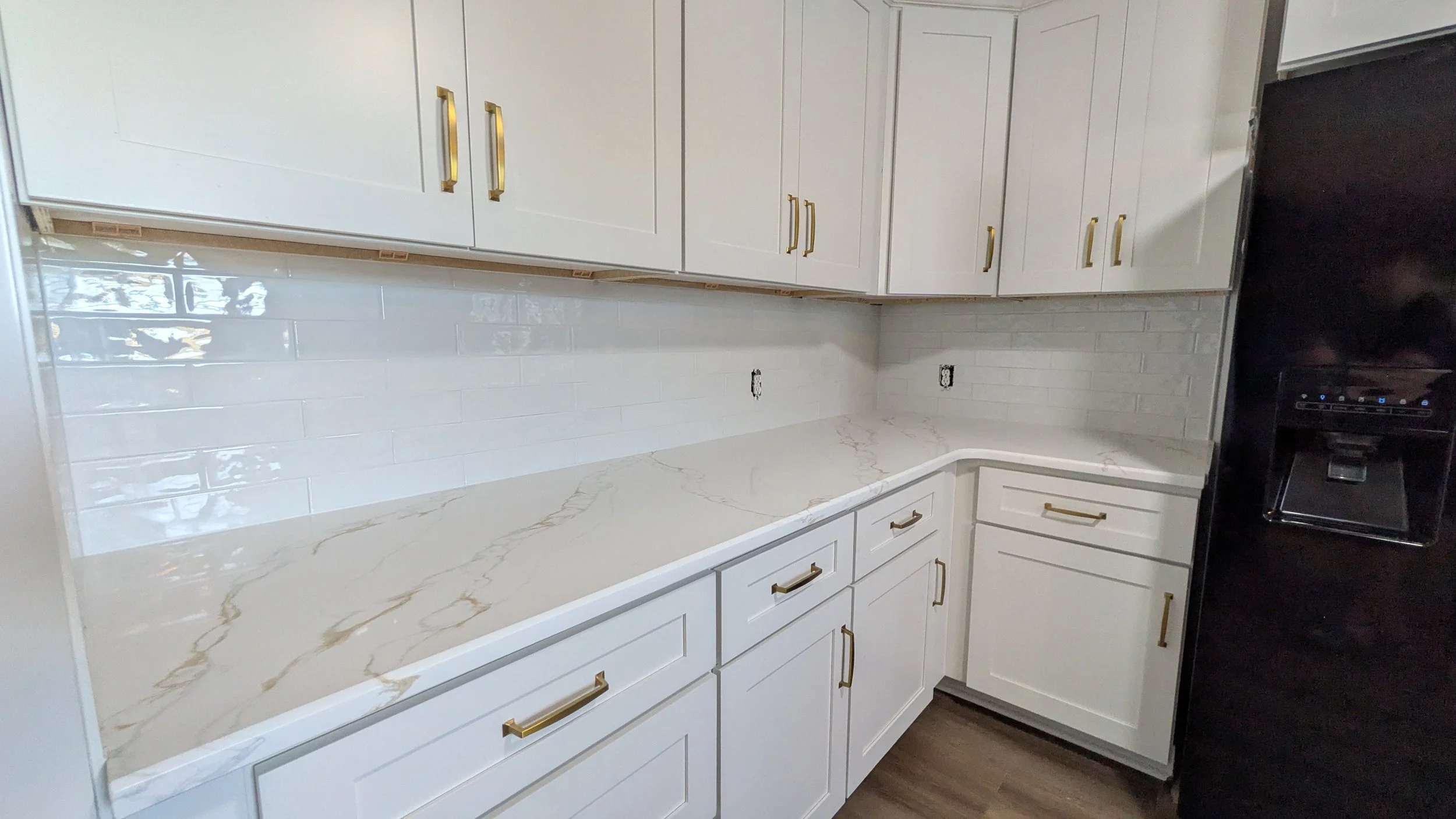 Kitchen with white cabinets, gold handles, marble countertop, white subway tile backsplash, and black refrigerator.