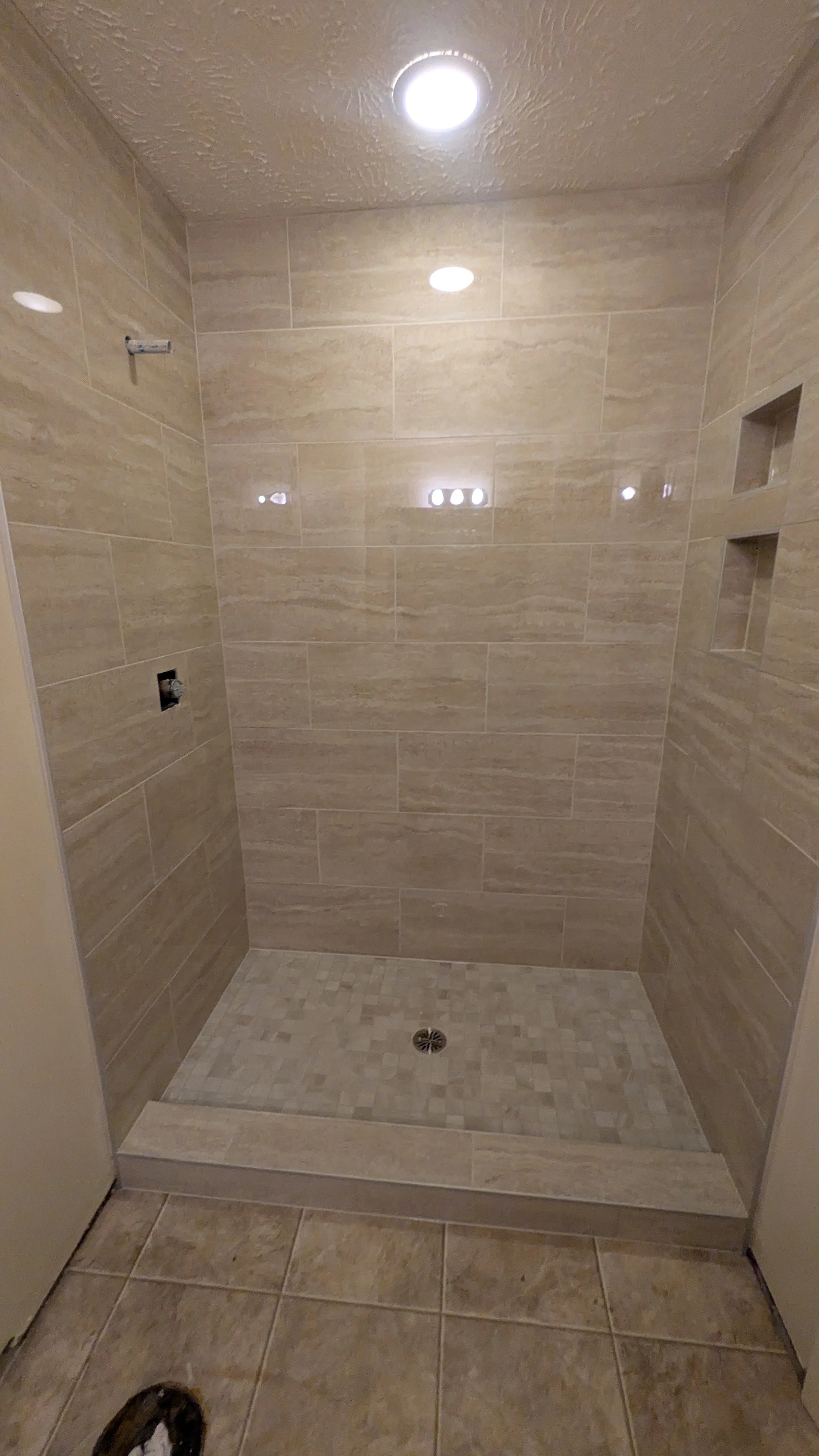 Empty shower with beige tiles, built-in wall niches, and a drain in the center of the floor.