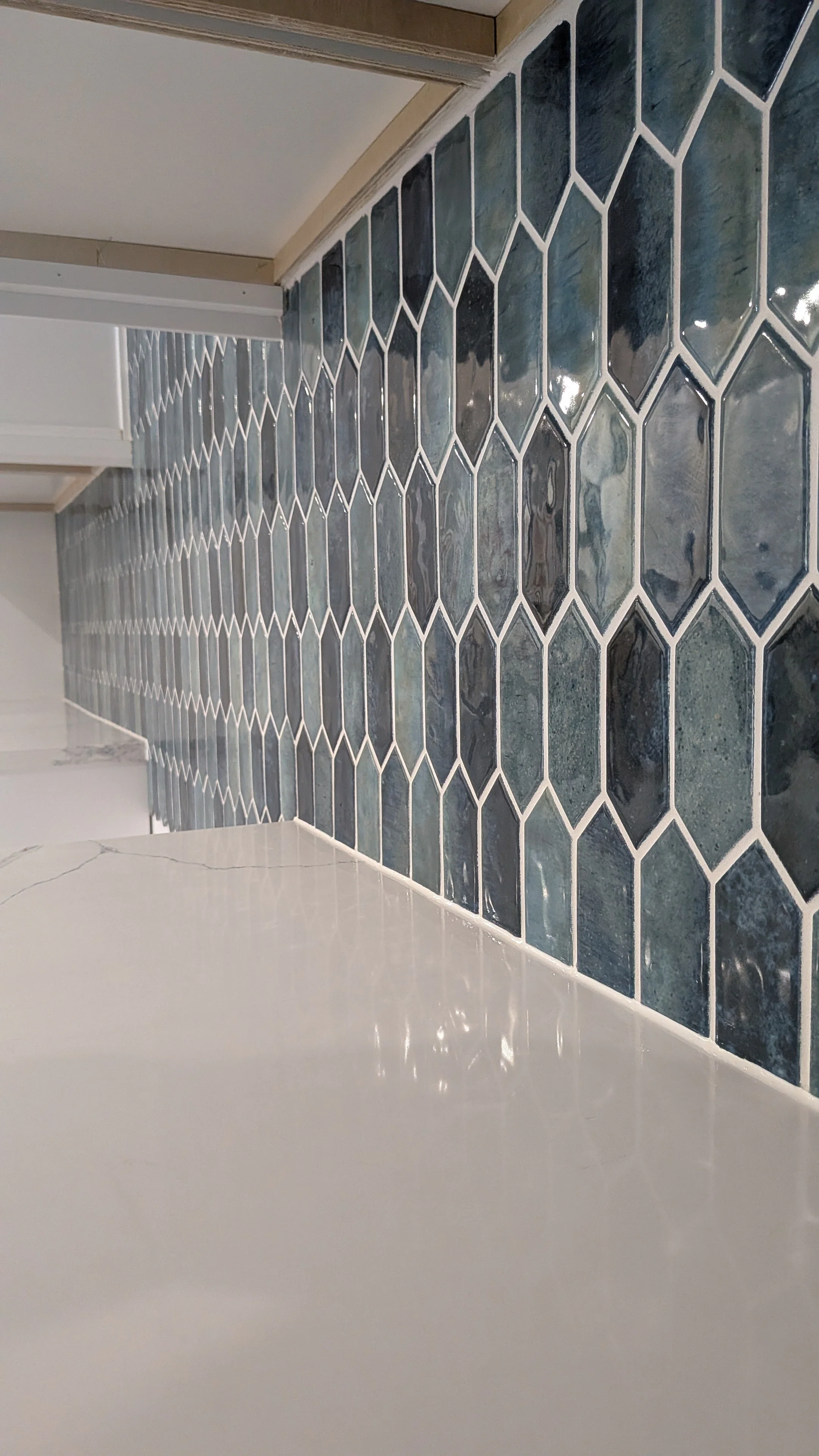 Close-up of a dark blue hexagonal tiled backsplash in a kitchen, with white grout lines, above a white countertop.