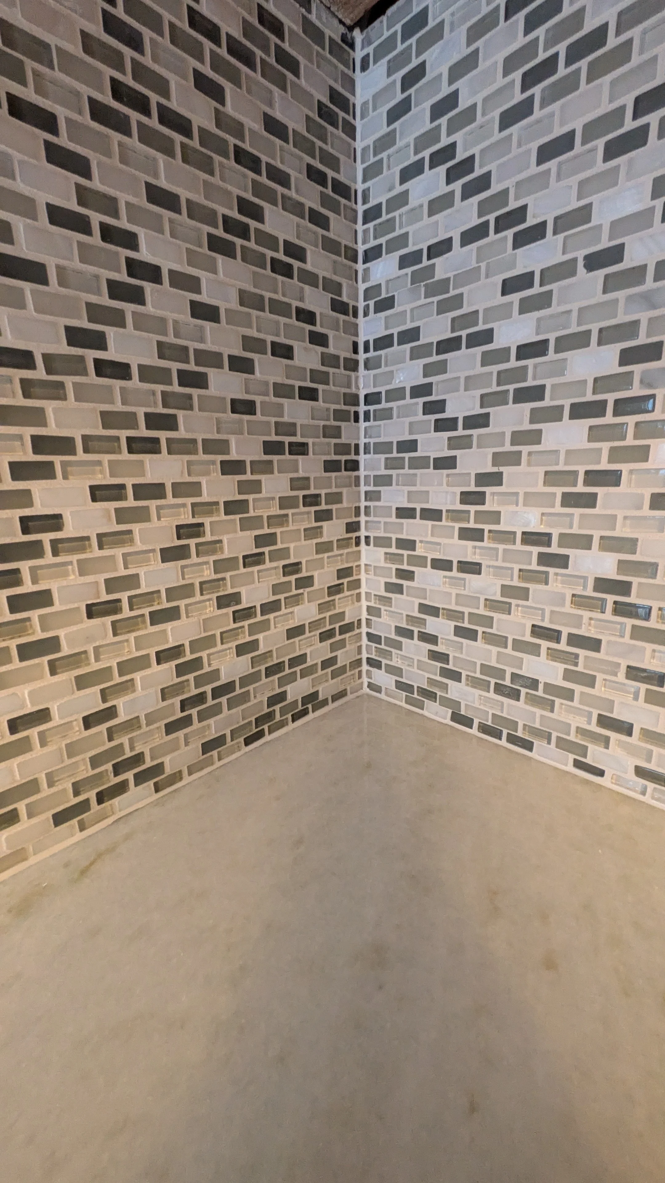 Corner of a room with modern gray brick wallpaper and a plain concrete floor.