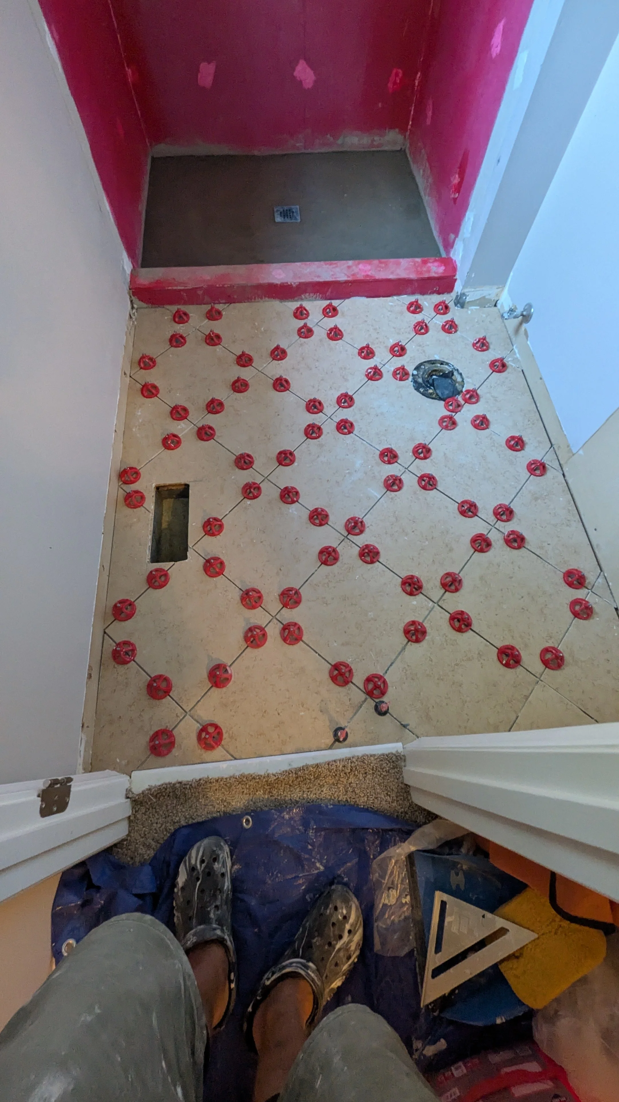 Bathroom floor construction with red spacers between tiles, a floor drain, and a hole for a toilet.