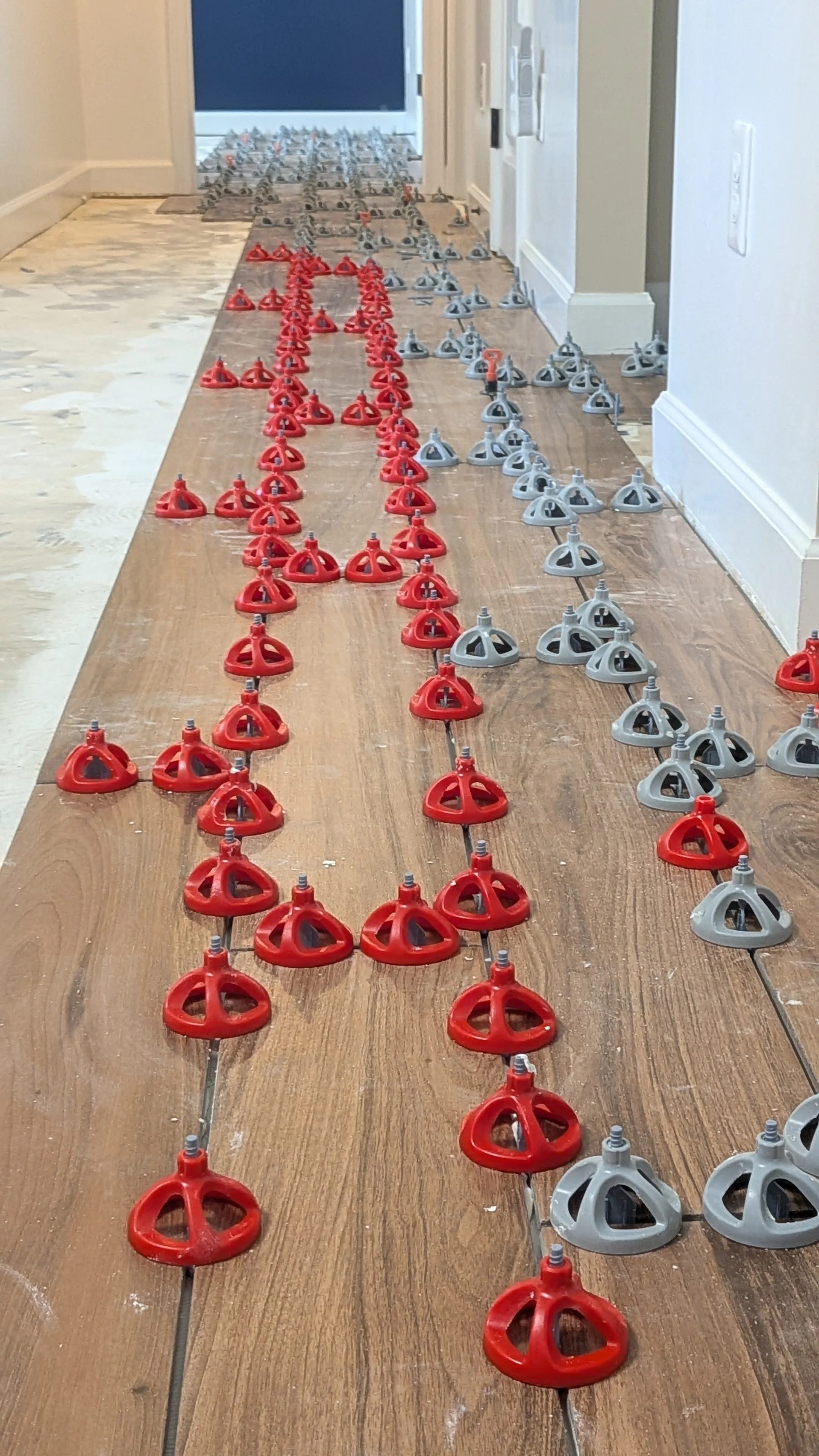 Rows of red and gray plastic leveling tools arranged on a wooden floor, likely for flooring installation.