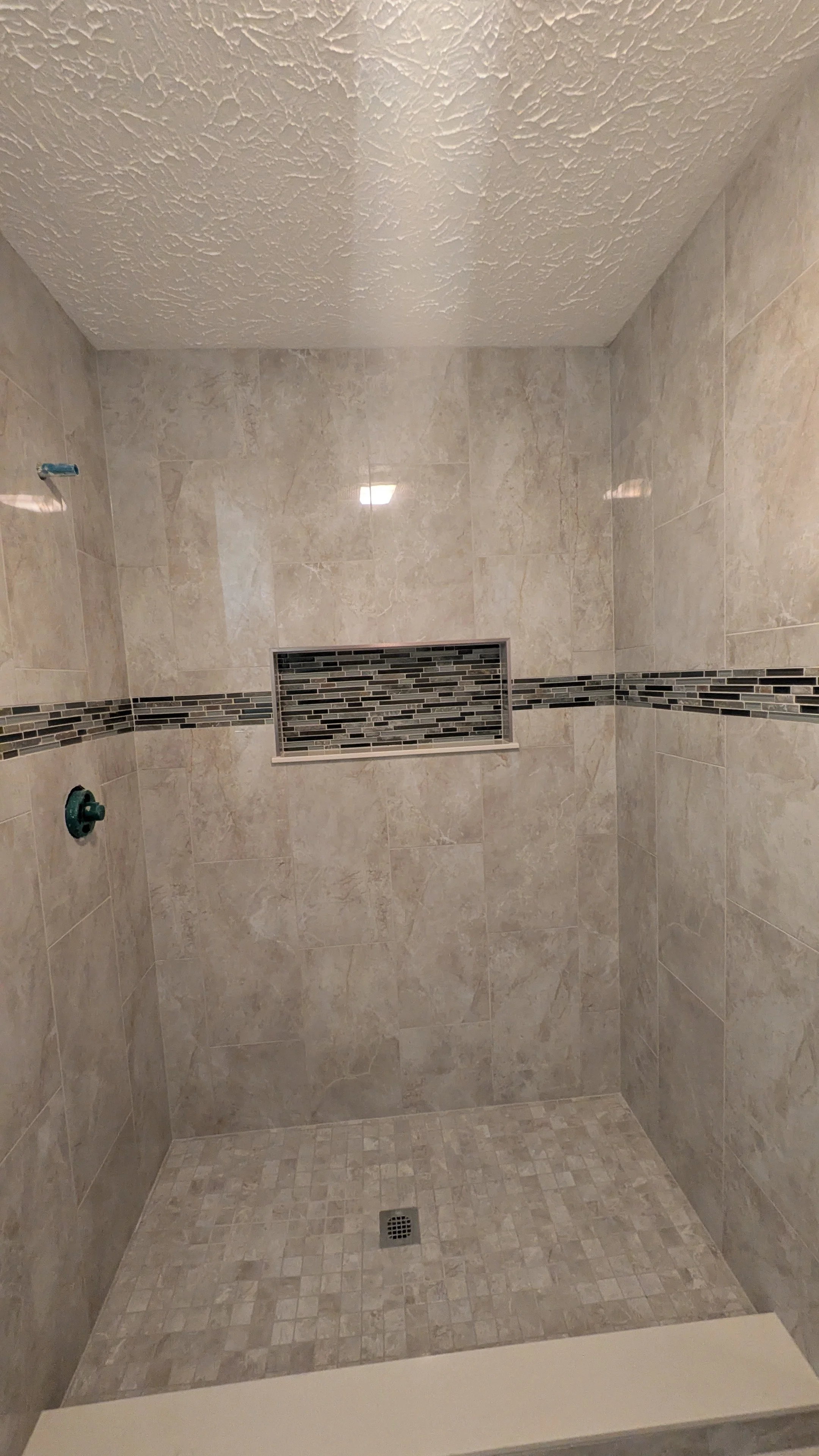 Empty shower with beige tile walls, a decorative tile strip, a built-in tiled shelf, and a tiled floor with a drain.