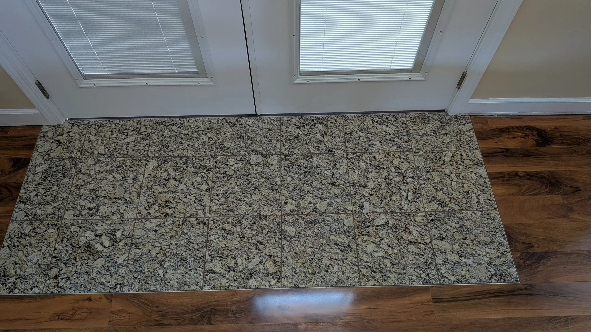 Entrance with granite tile floor and double white glass doors with blinds.