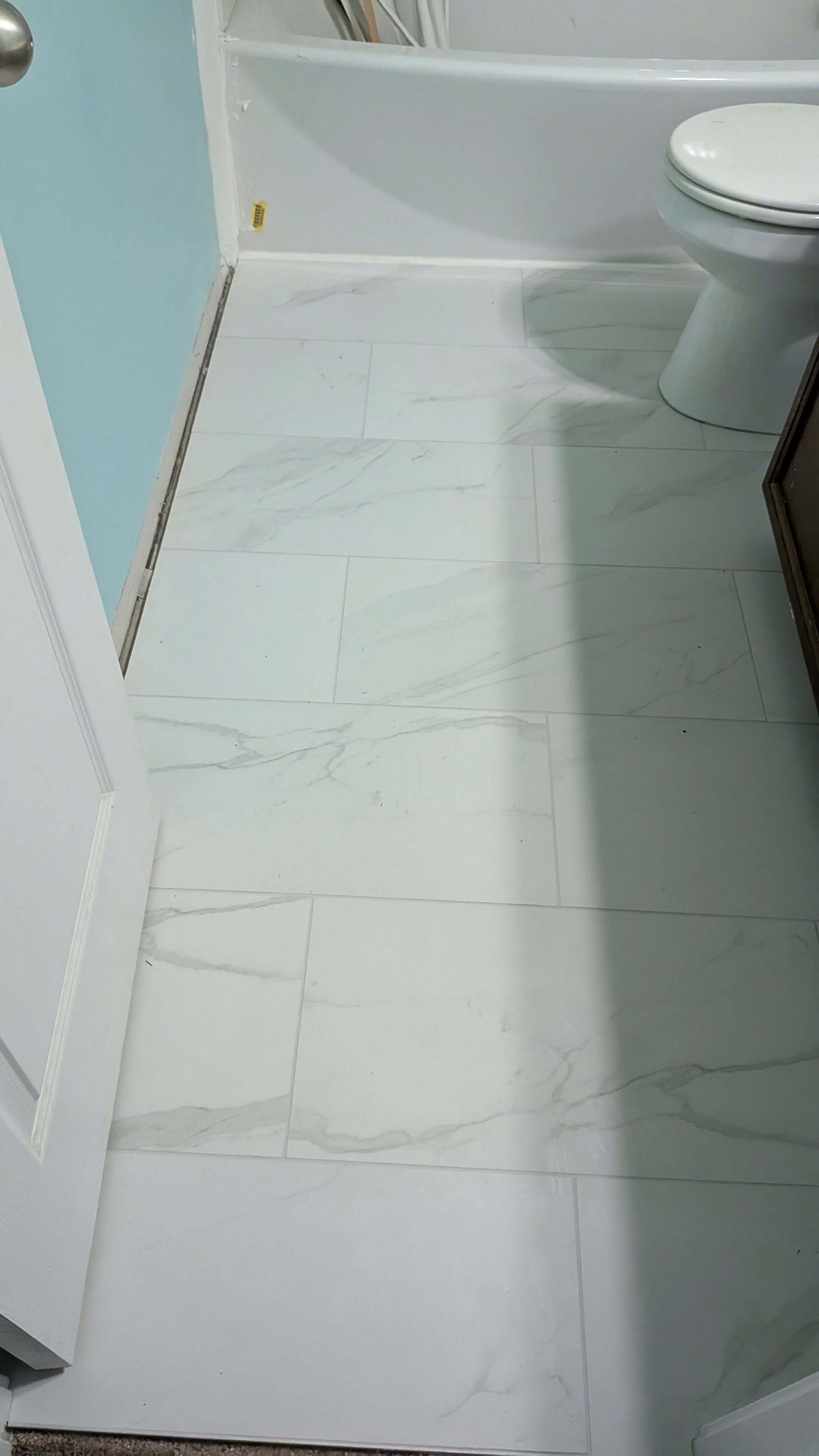 A bathroom with white marble tiles on the floor, a white toilet, and part of a white wall with light blue paint.