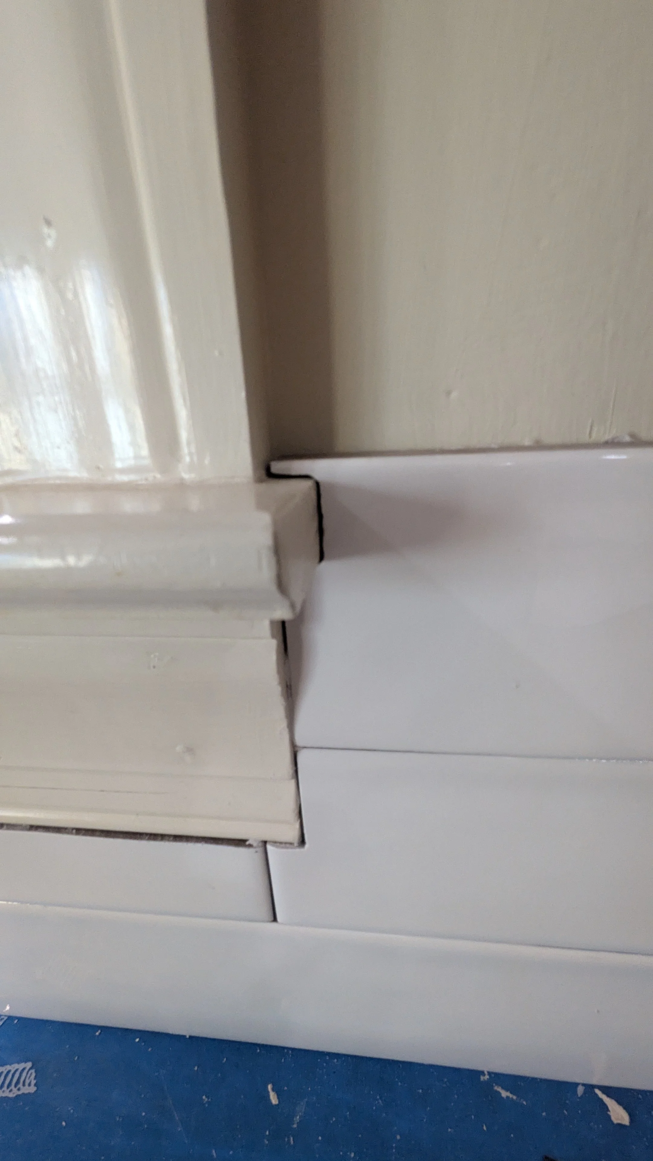 Close-up photo of a door frame with a gap between the door and the frame, showing damage or separation at the corner.