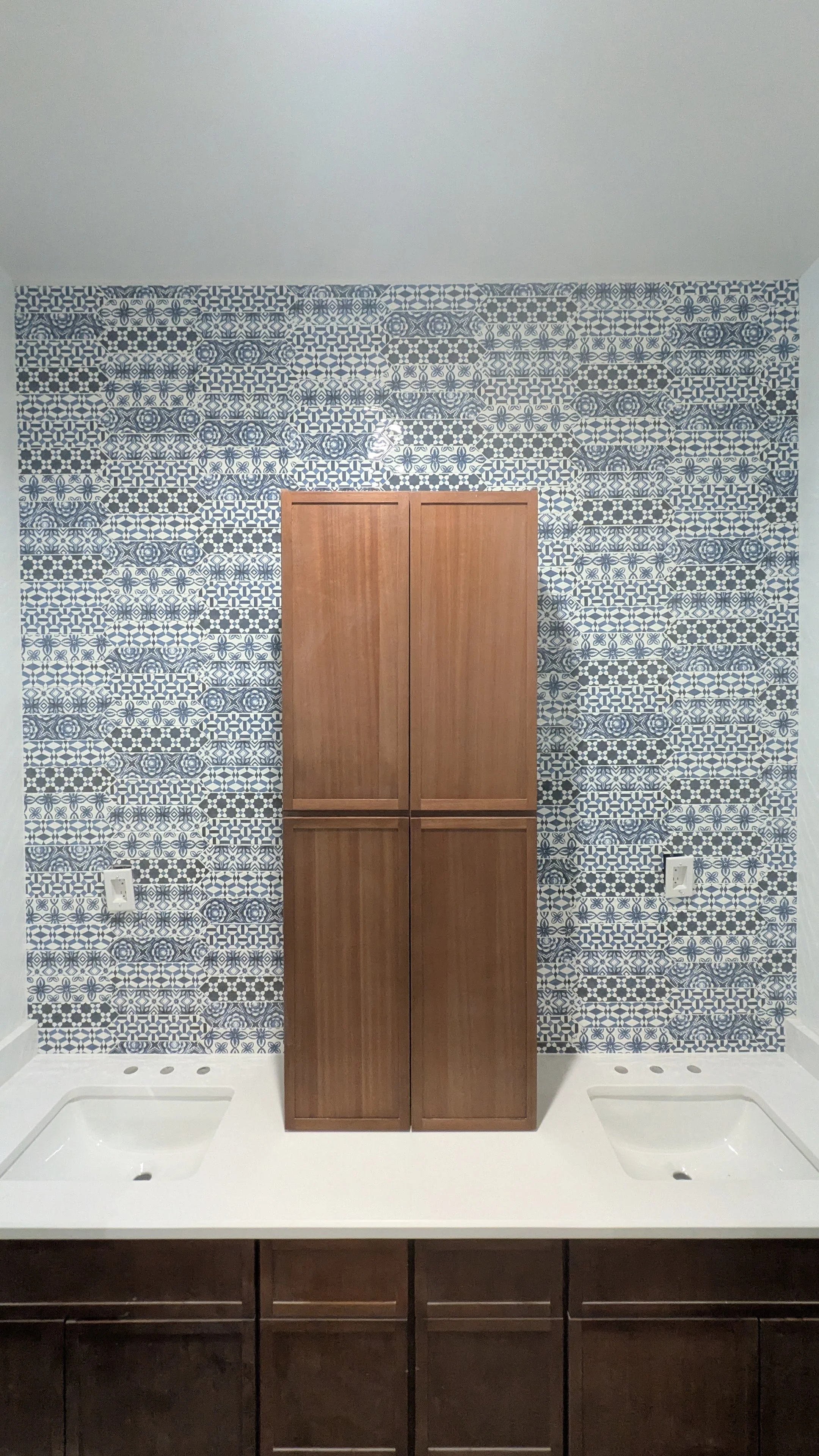 Bathroom vanity with two sinks, wooden cabinets, and a patterned blue and white tiled wall.