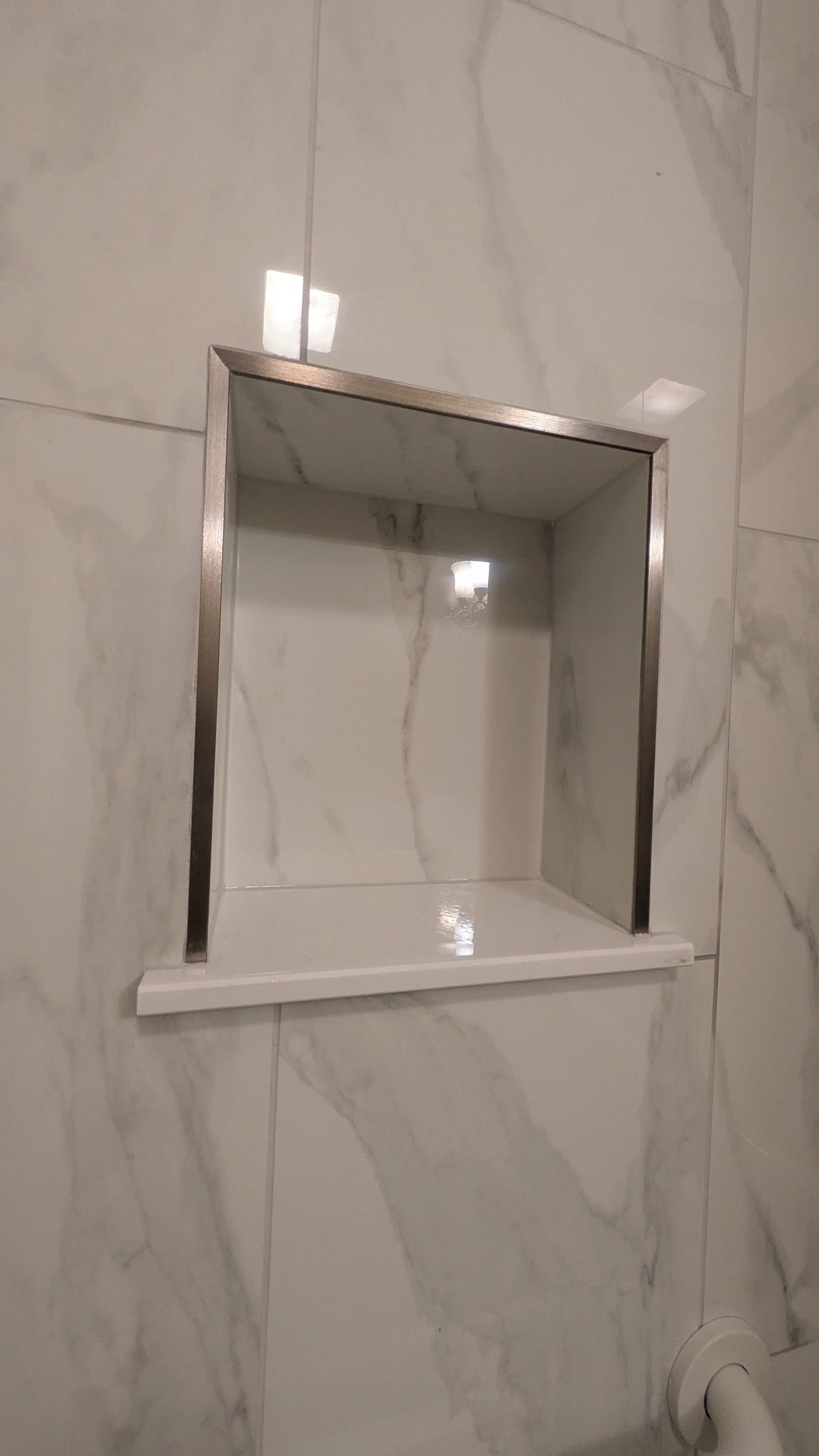 Built-in tile shower shelf with metal frame, empty and mounted on marble wall.