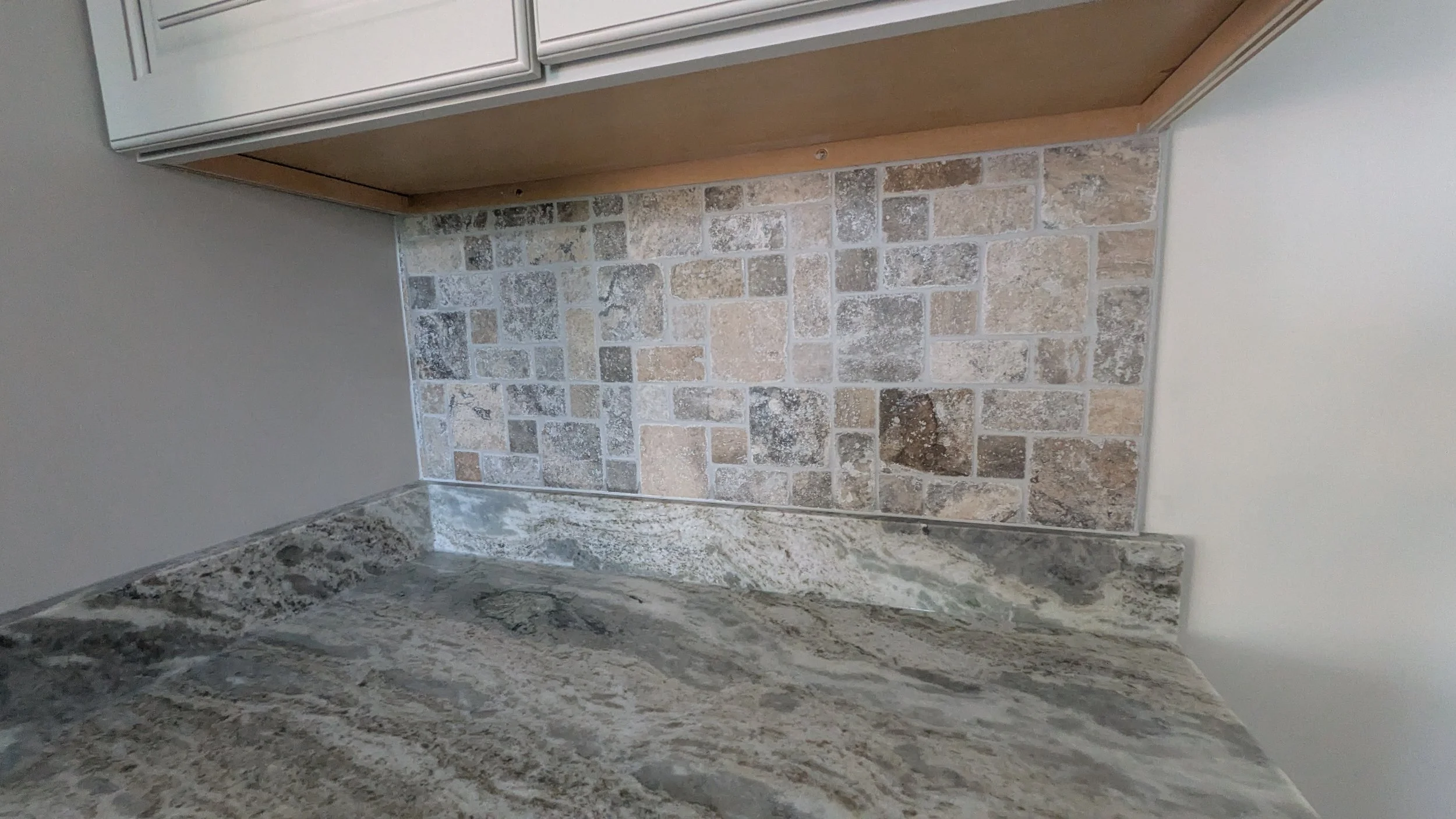 Close-up of a kitchen backsplash with square stone tiles and a granite countertop.
