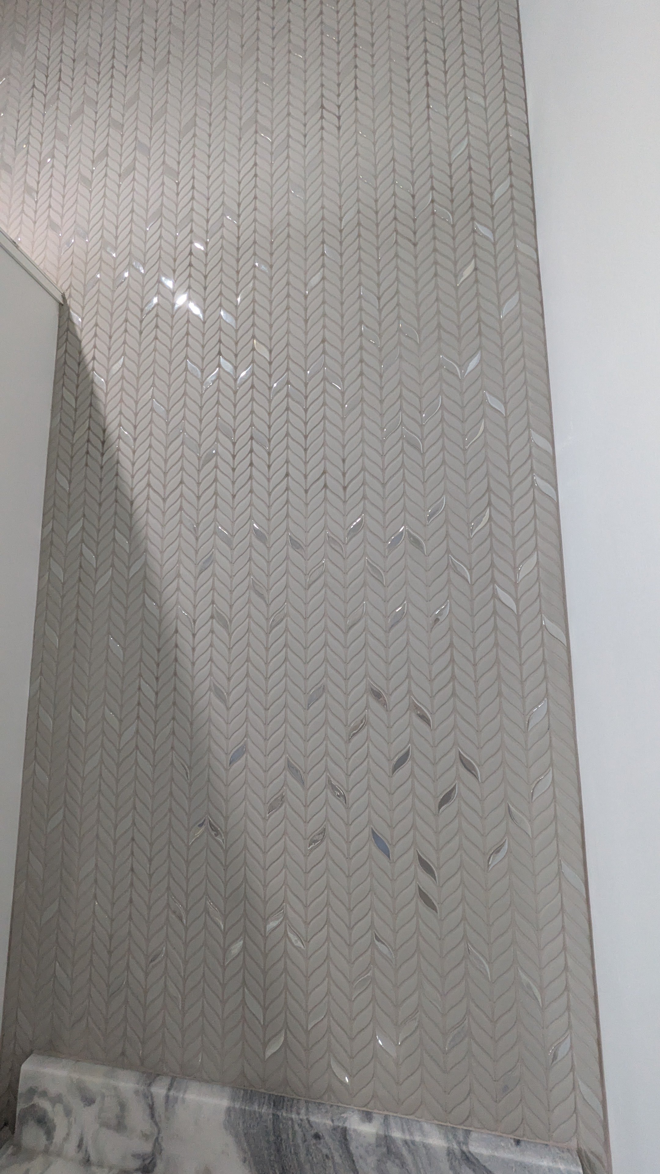 Close-up of a decorative exterior wall with a textured, patterned surface featuring leaf-shaped cutouts, on a marble base.