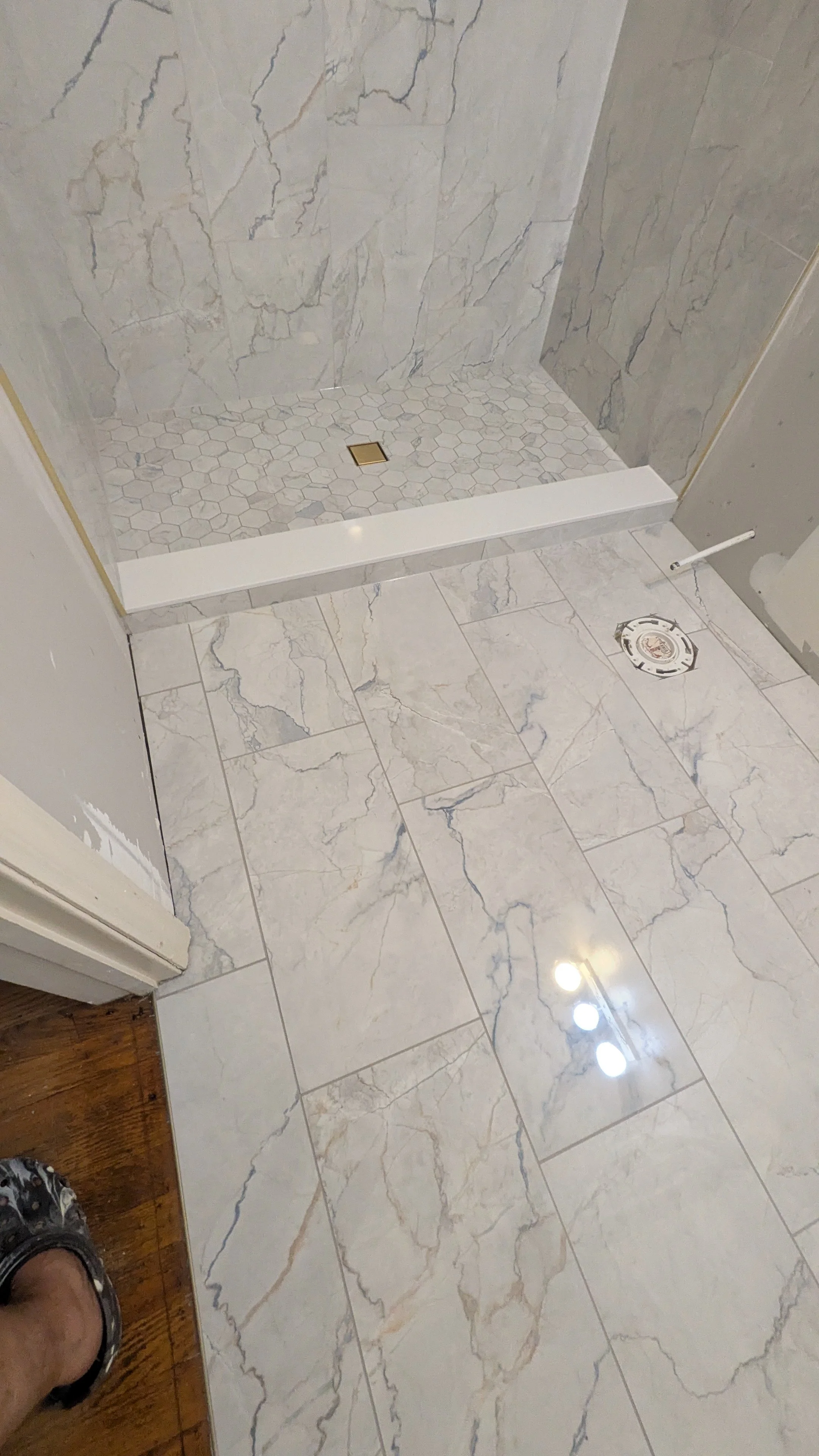 Bathroom with marble tile floor and a shower area with marble tile walls and a hexagonal tile shower floor, plumbing fixtures and an air vent on the floor.
