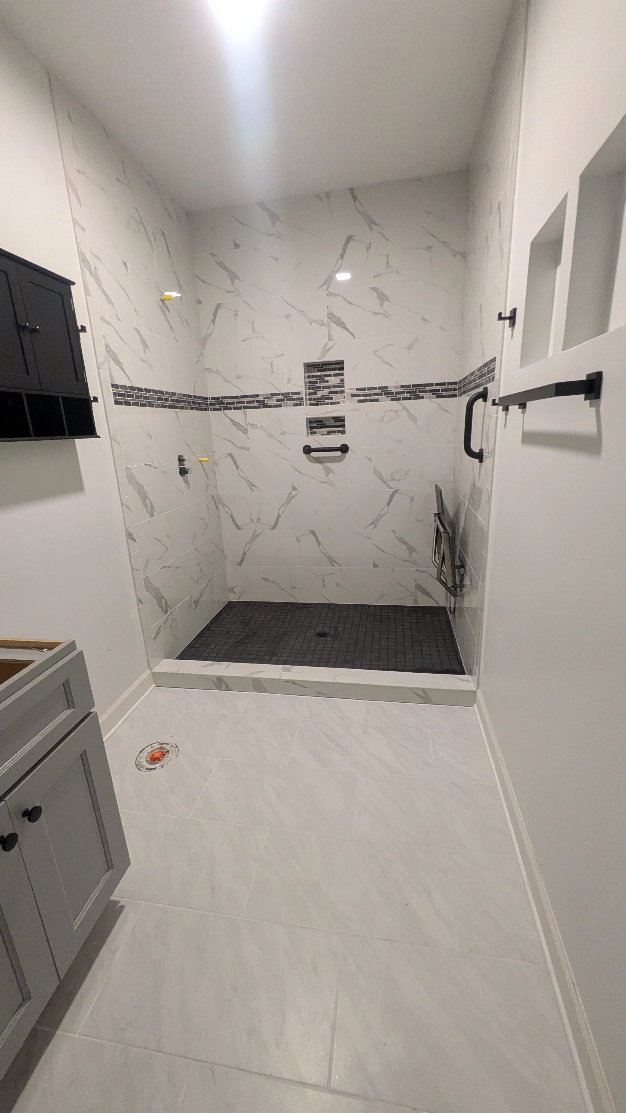 Bathroom with a walk-in shower, white marble tiles, black accents, a black cabinet, and a grey vanity.