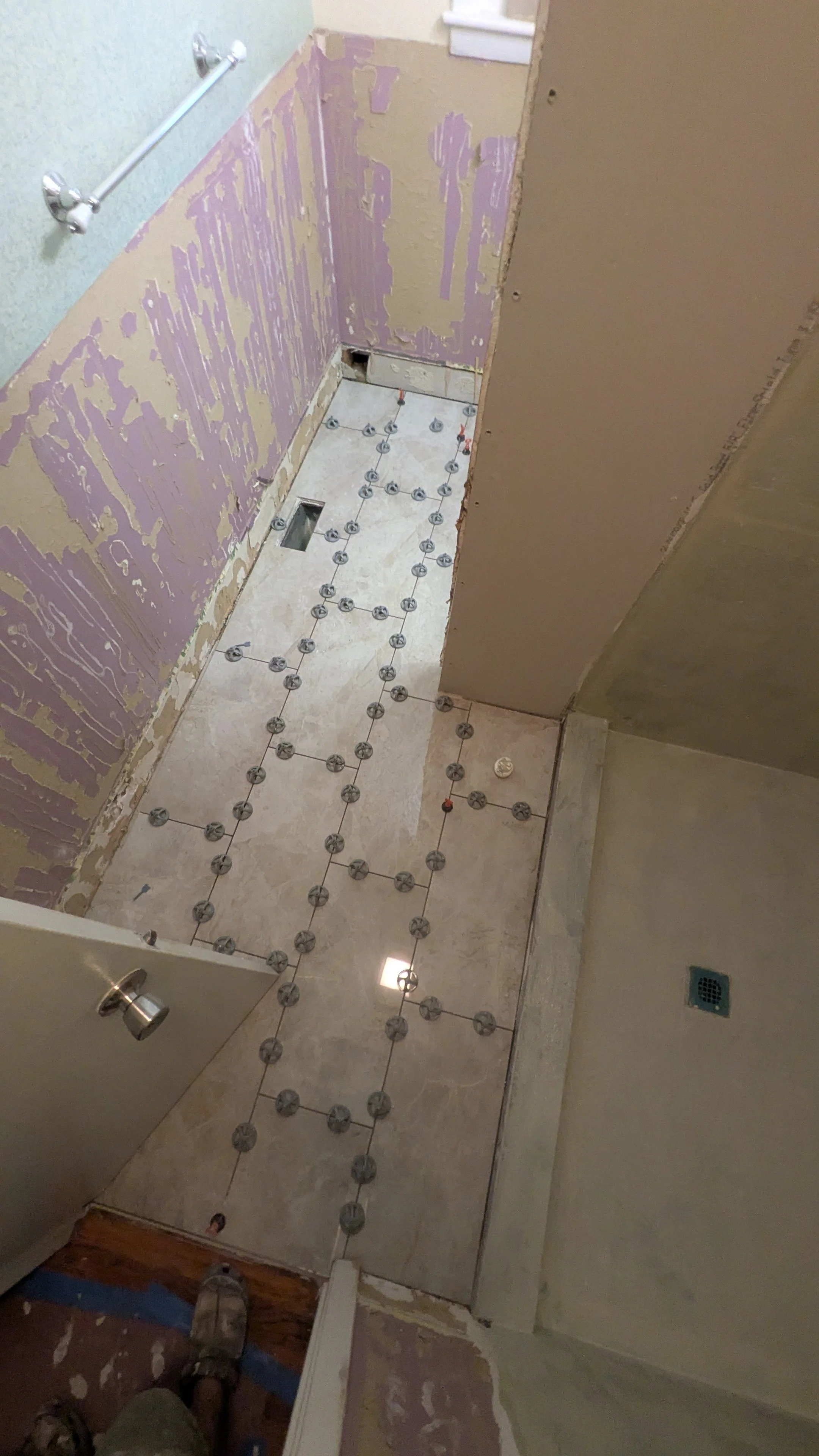 Bathroom under renovation with tile flooring installation in progress, exposed drywall, and construction materials visible.