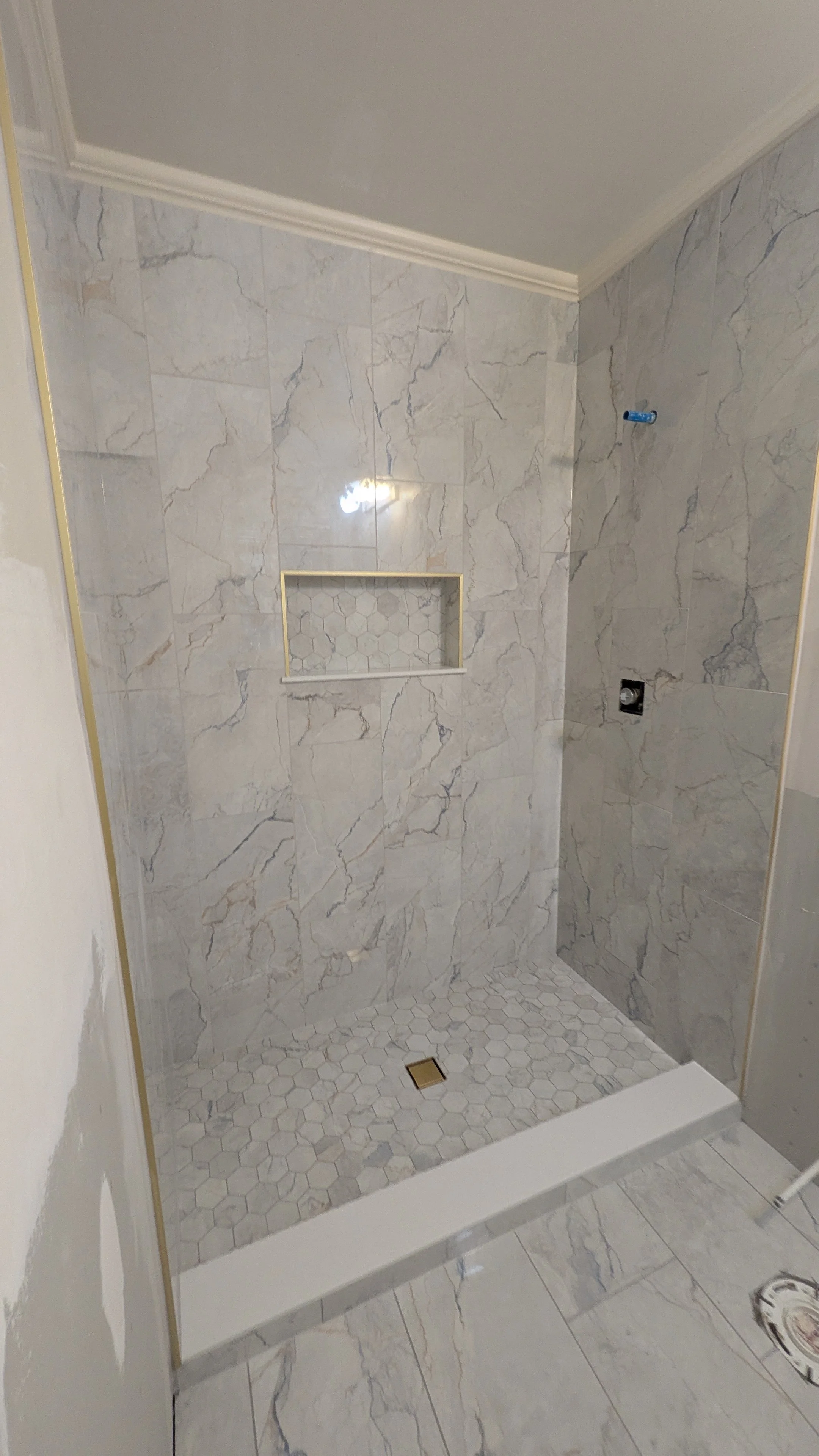 Empty shower with marble tile walls, a built-in niche, hexagon tile floor, and a drain.