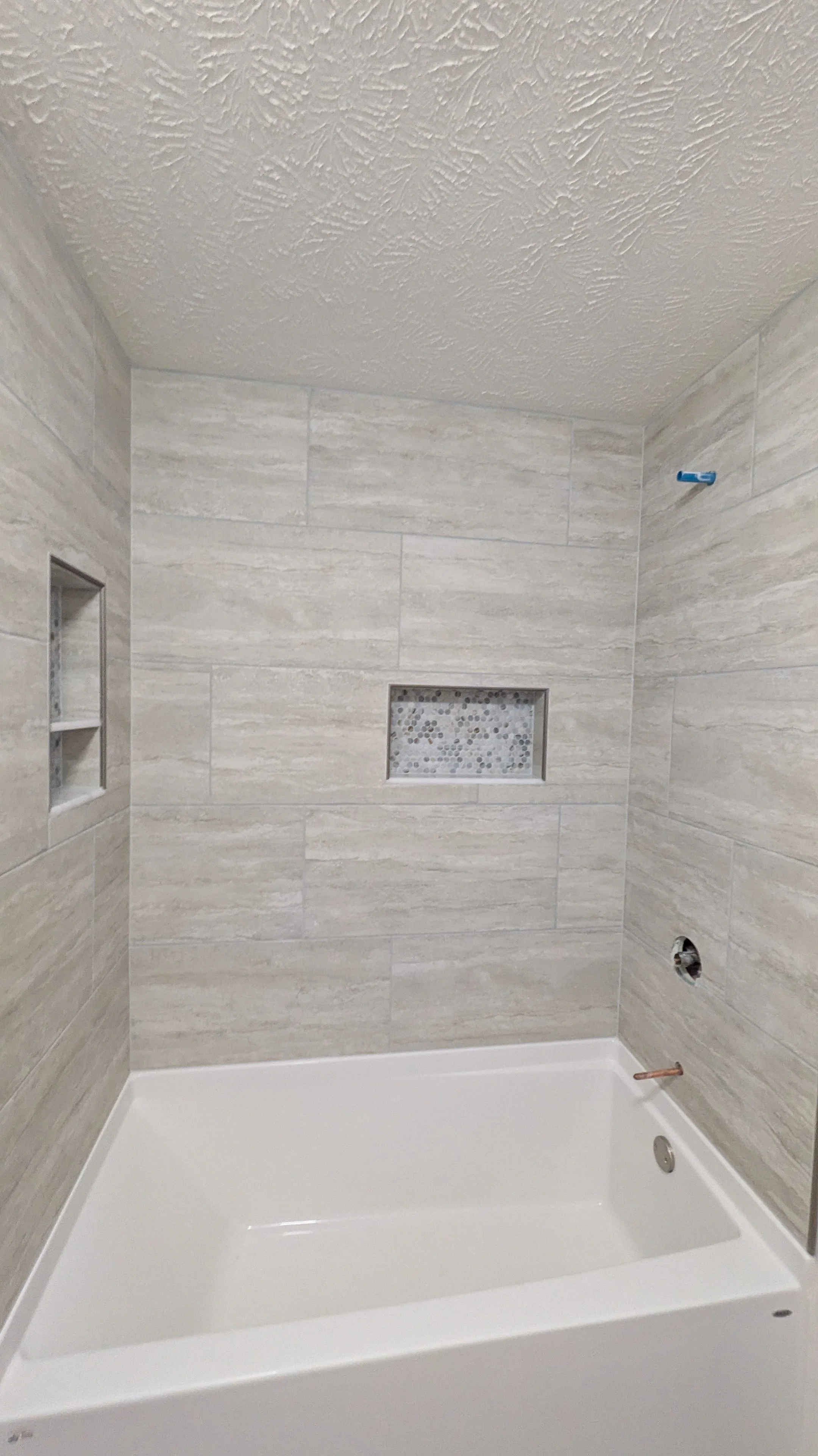 Newly installed bathroom shower with beige tiled walls, a built-in niche with pebble tile, no showerhead or fixtures yet