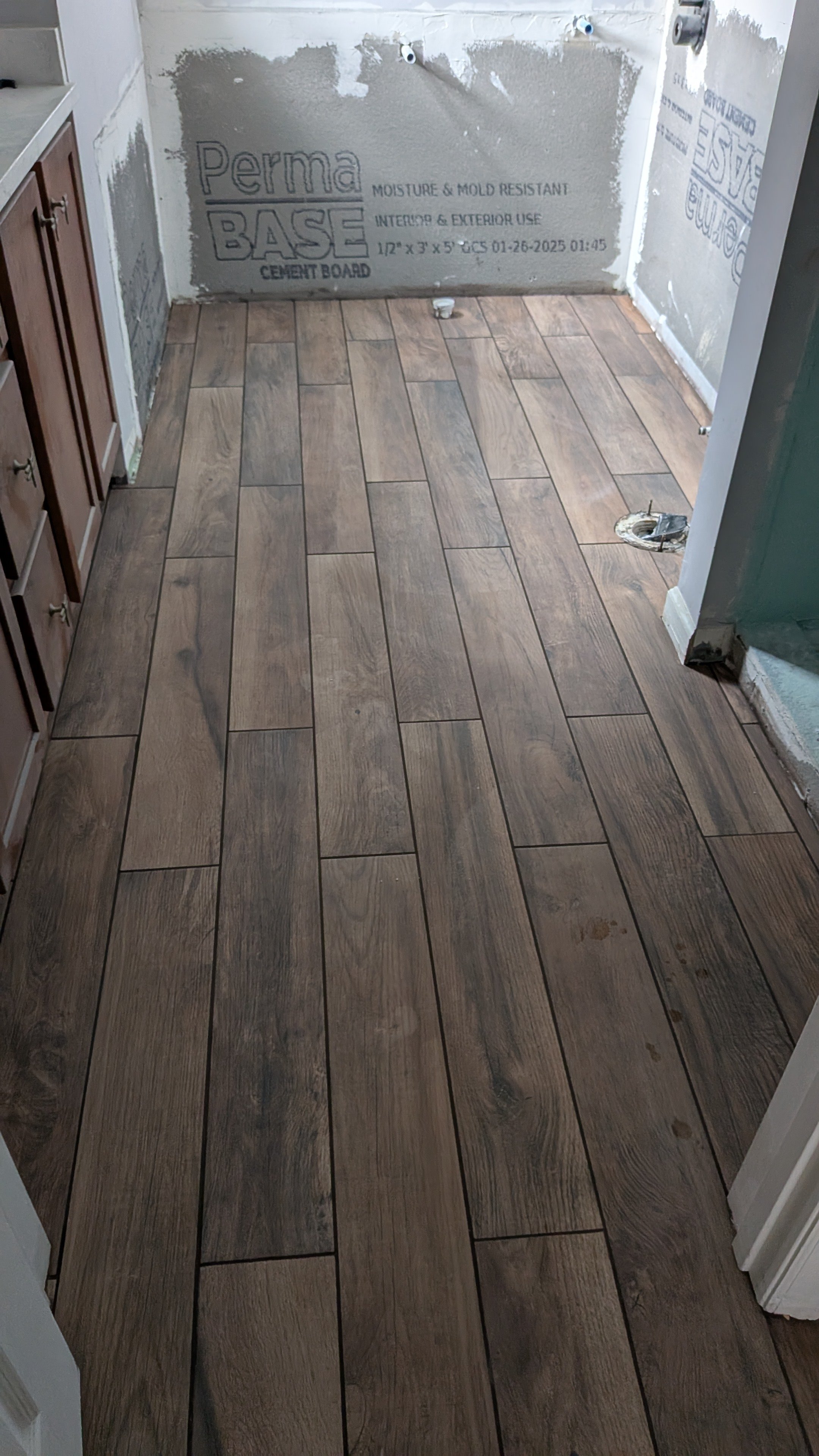 A room with new wood-look tile flooring, partially finished with construction materials and unfinished wall surfaces.