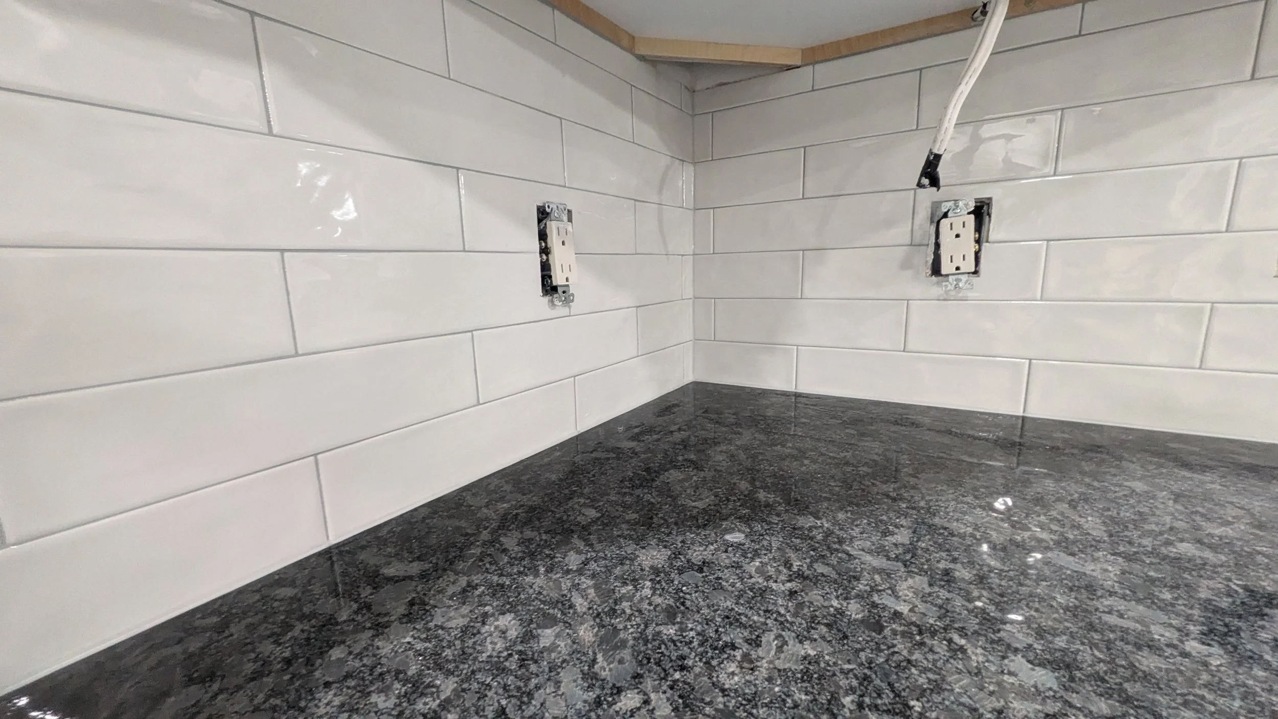 Empty kitchen countertop with partially installed electrical outlets and a white tiled backsplash.