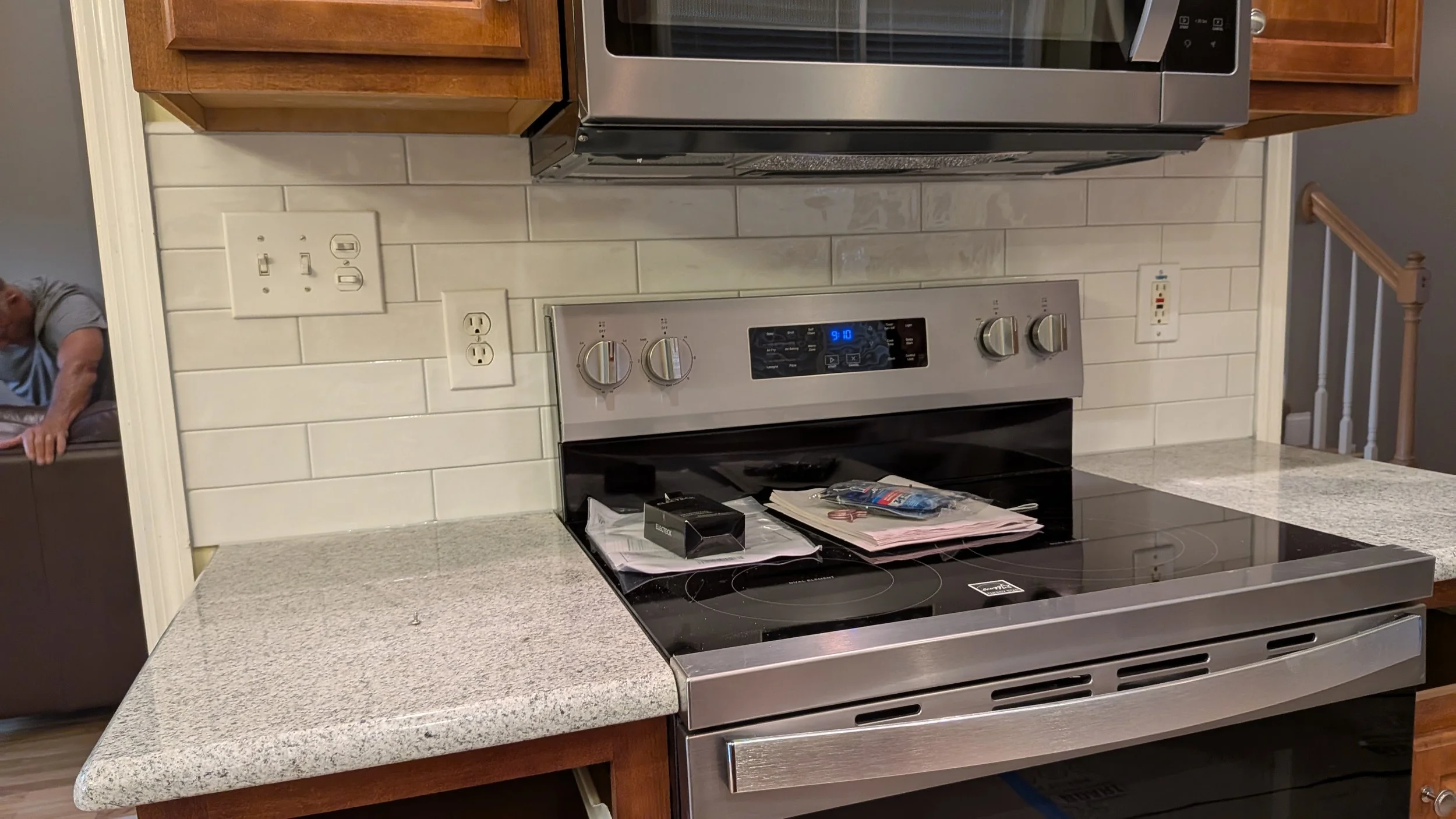 Kitchen stove with papers, a box, and small items on top, next to a granite countertop and a white tiled wall.