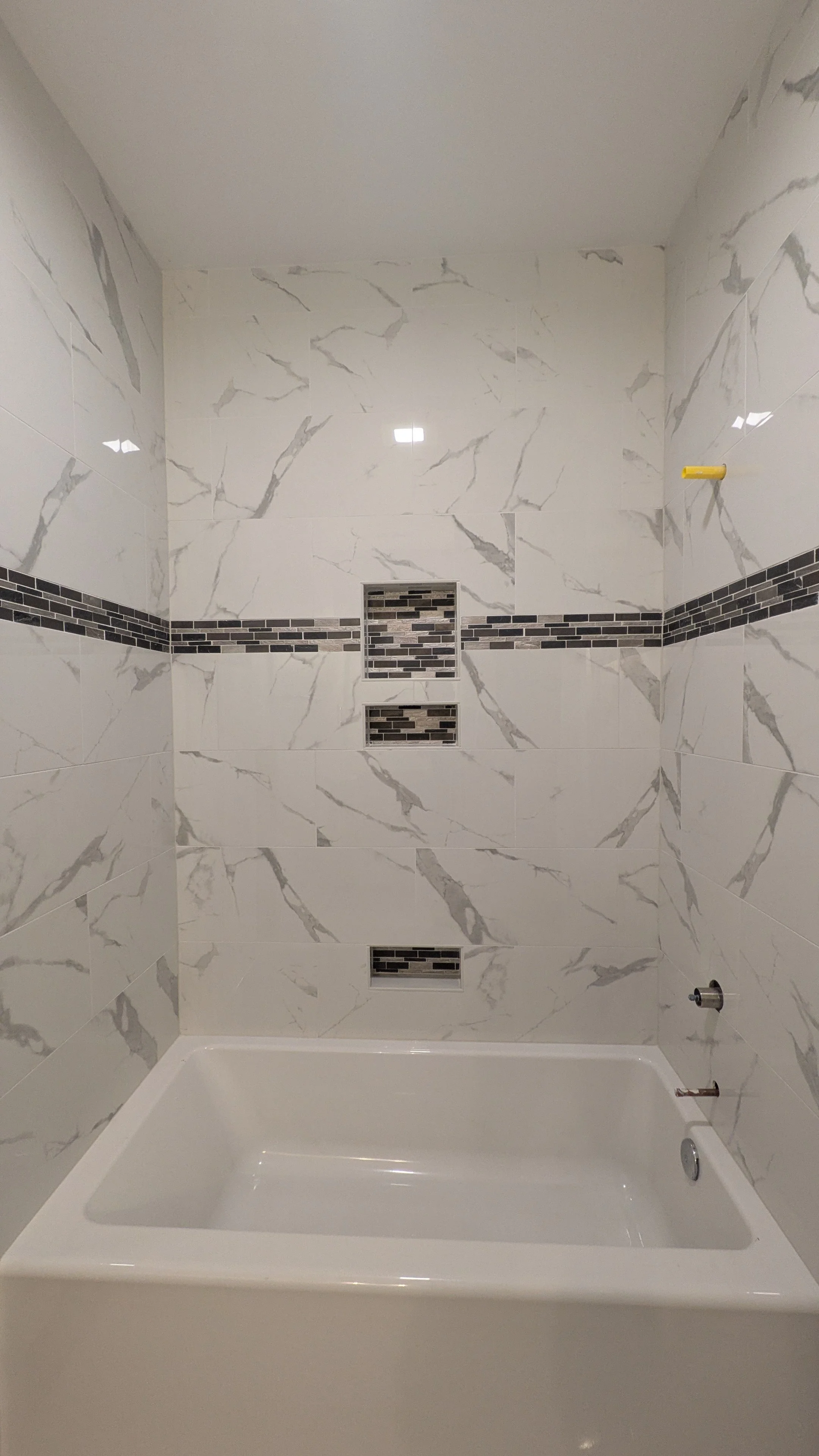 Bathroom with marble-like wall tiles, black and gray mosaic accents, a bathtub, and two built-in shower niches.