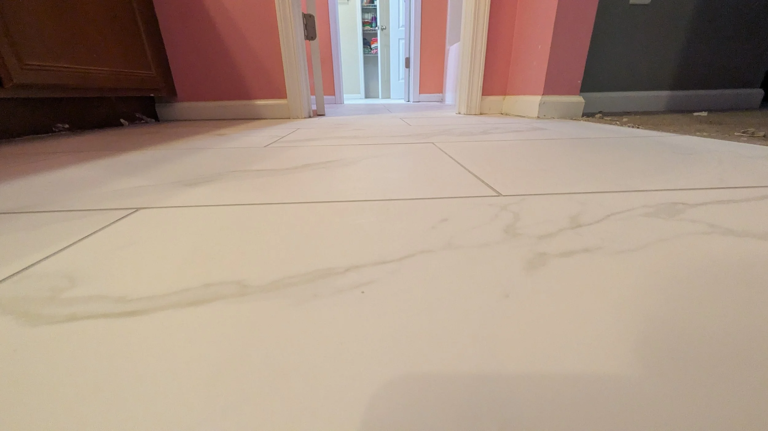 Low-angle view of a tiled kitchen floor with open bathroom cabinet door in the background.