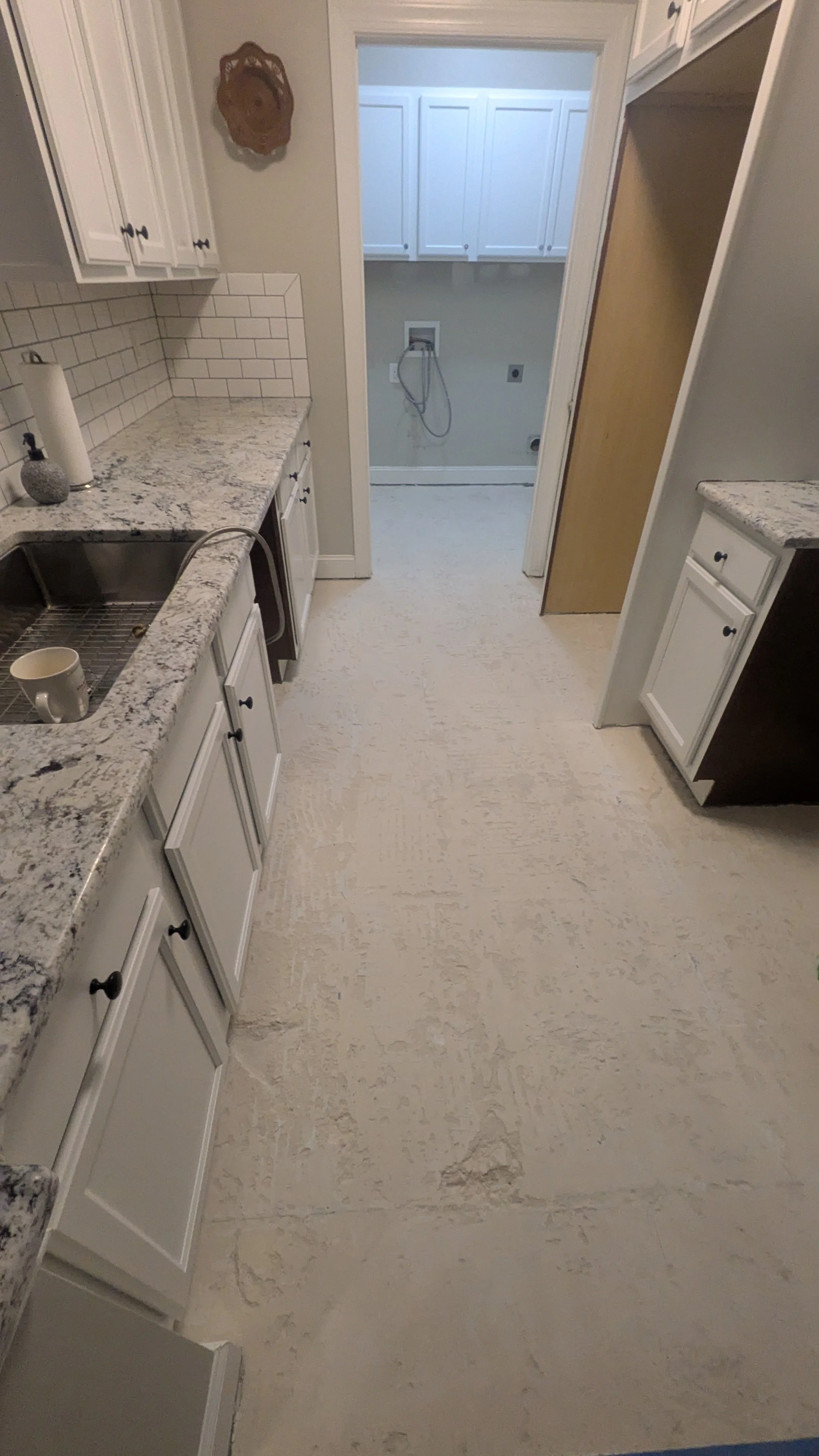 A kitchen with white cabinets, granite countertops, a sink with a mug, and an adjacent laundry room with white cabinets and laundry hookups.