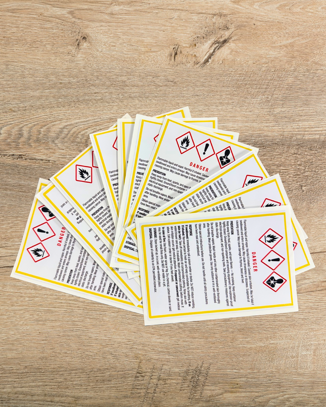 Pile of warning labels or safety stickers with hazard symbols on a wooden surface.