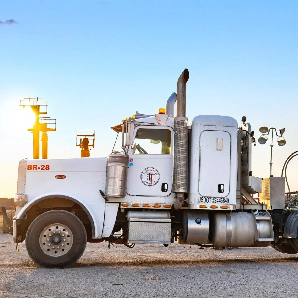 White semi-truck parked on a lot at sunset with utility poles and lights in the background.