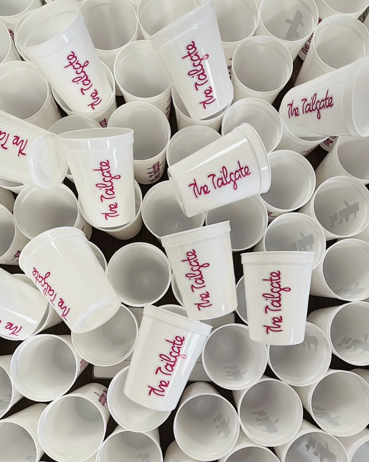 Numerous white cups with pink text reading 'The Tailgate' scattered across a surface.