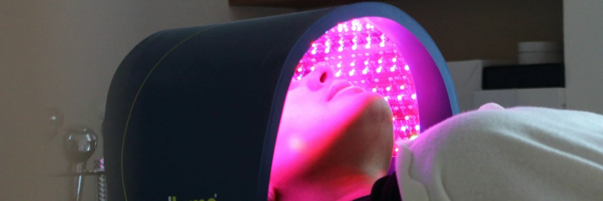 Person lying inside a UV light therapy device with pink glow, used for skin treatment.