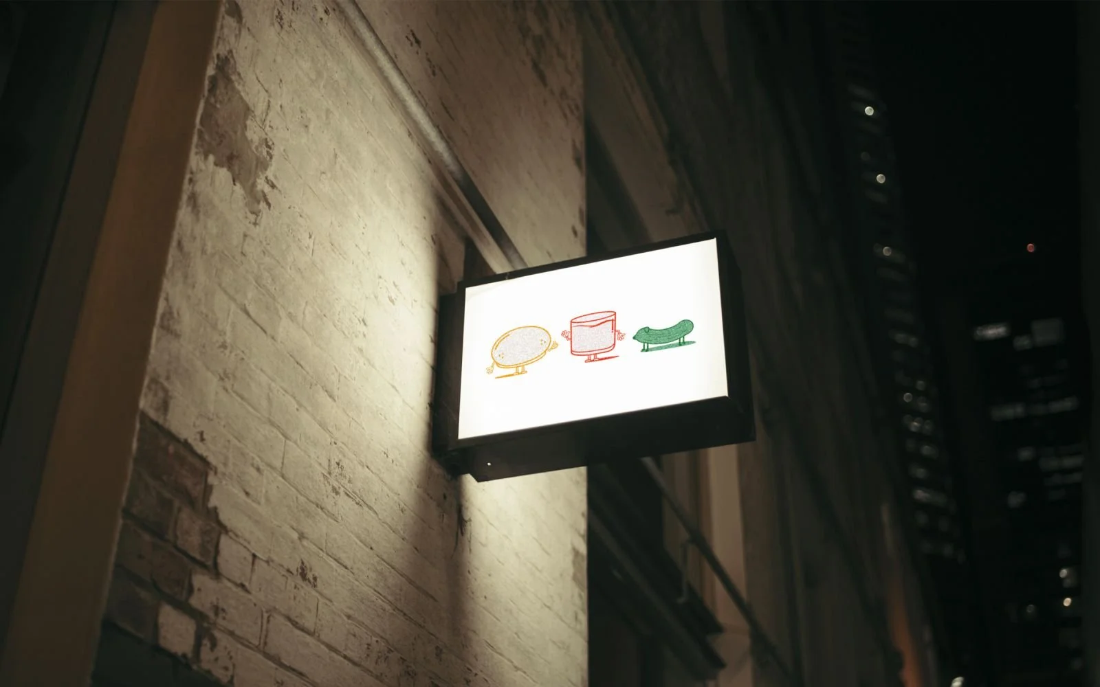 Illuminated shop sign at night for a Washington DC creative studio, featuring playful lemon, coffee cup, and leaf icons, representing the brand’s social impact merchandise focus