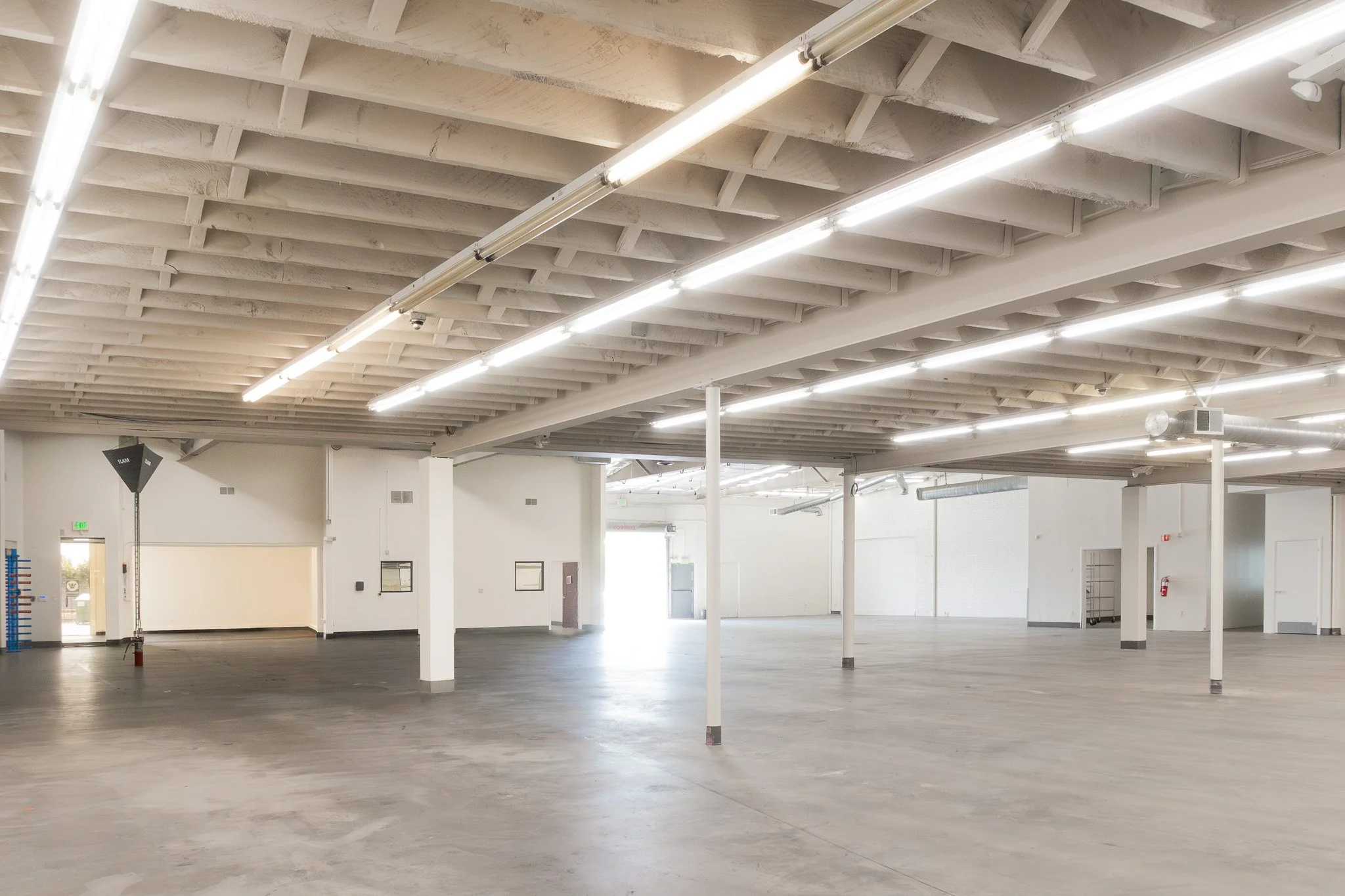 Empty commercial space with high ceilings, bright lighting, and concrete floors.