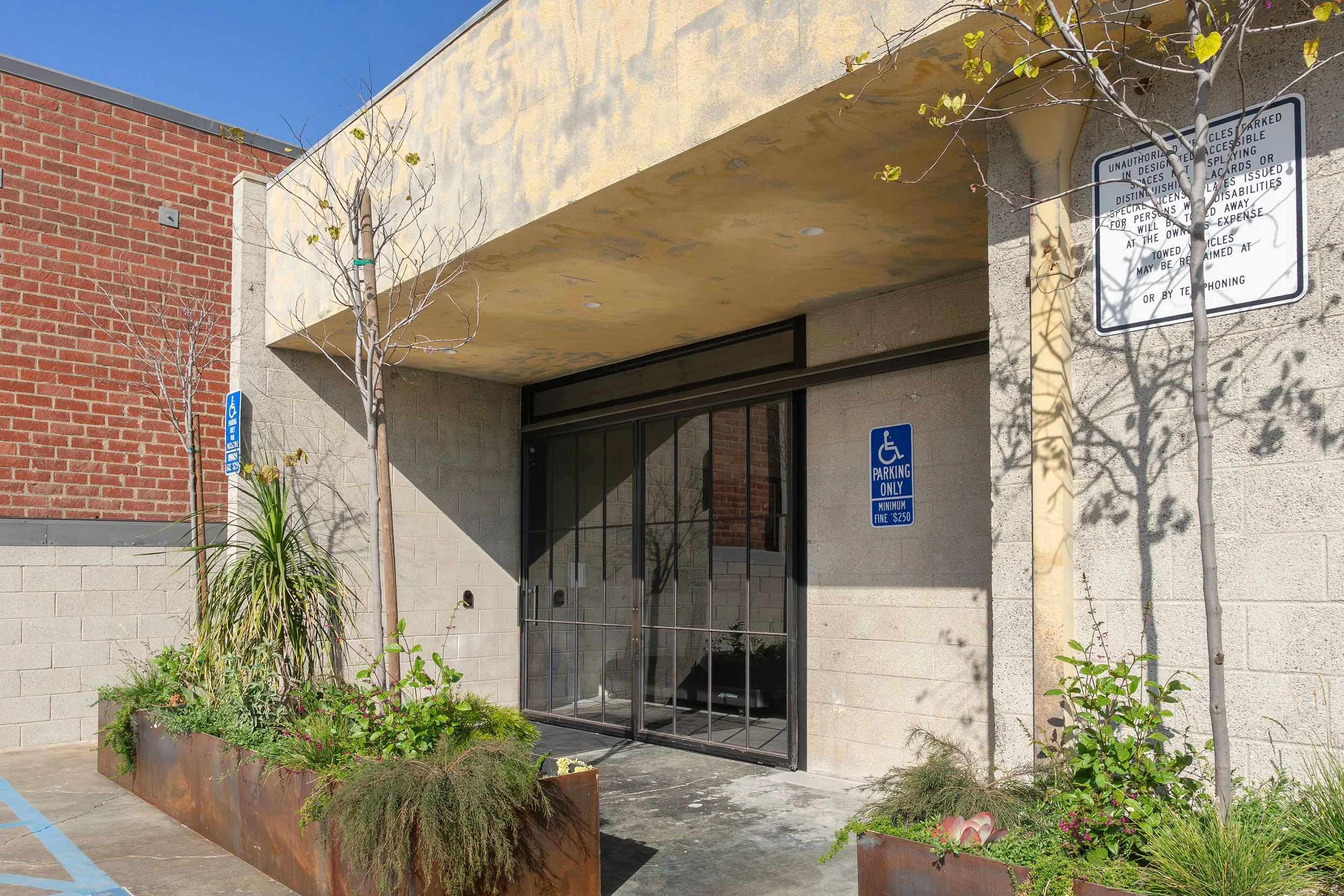 Building entrance with glass doors, two small trees, and signs indicating handicapped parking and restrictions.