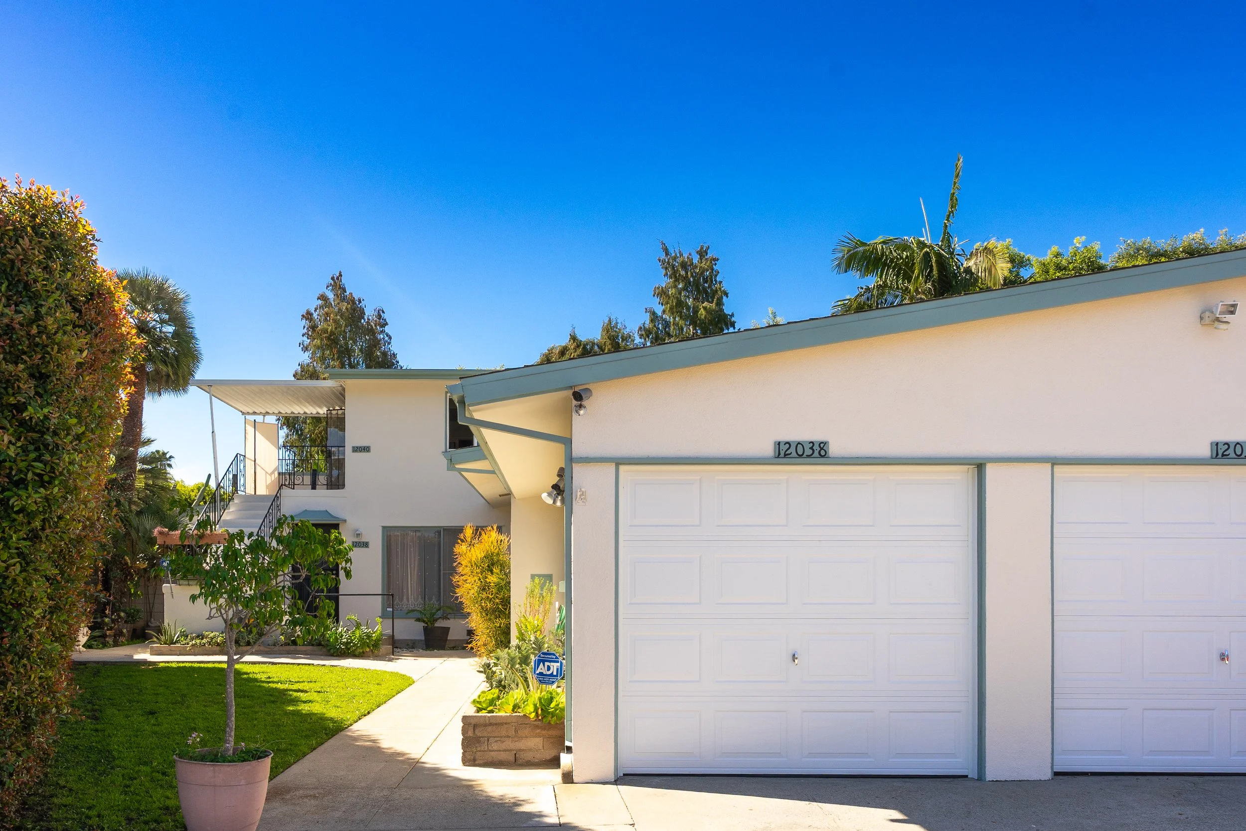 Front view of a two-story white house with a garage and a small garden under a clear blue sky.